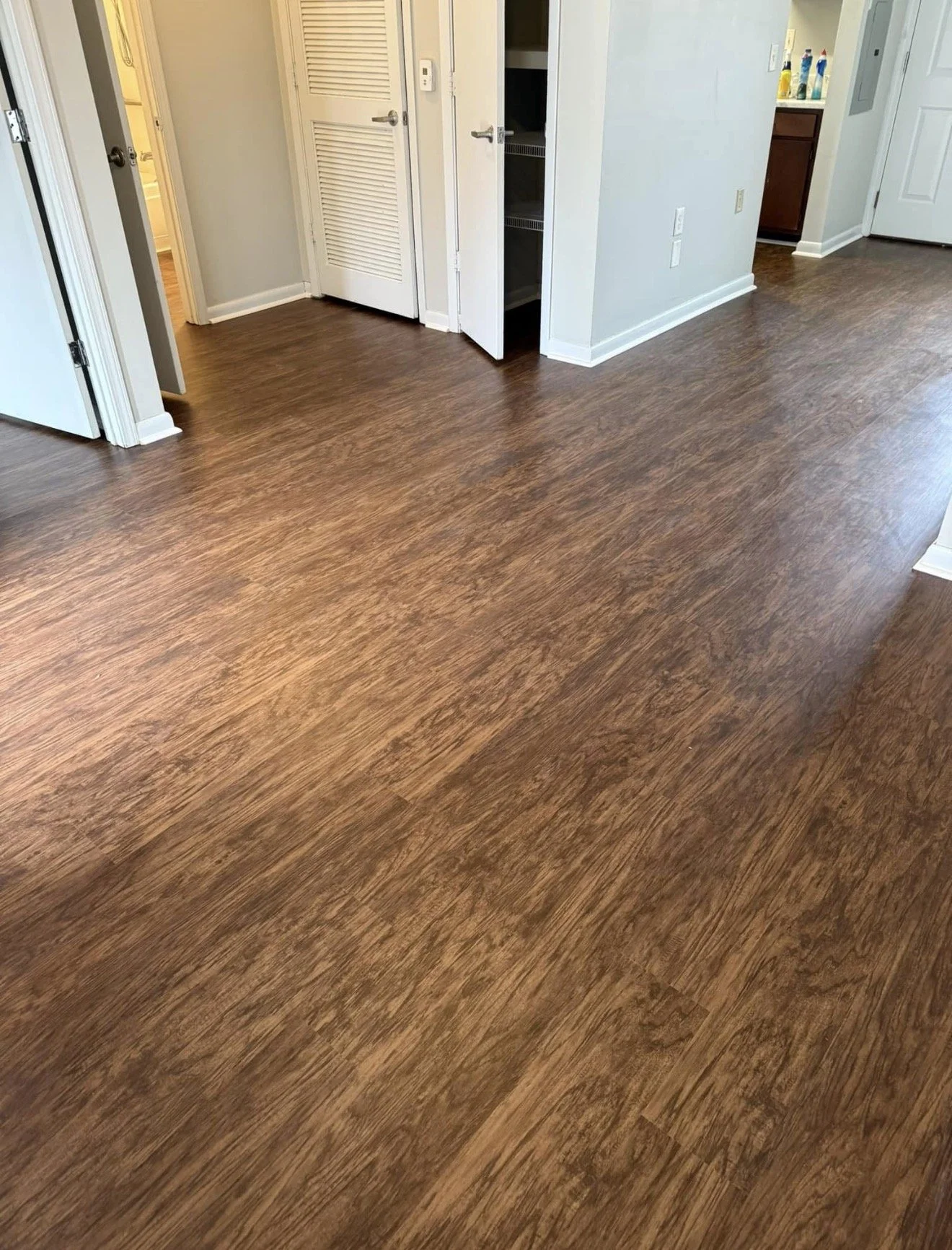 A room with brown wood flooring, white walls, and multiple doorways leading to other rooms, including a bathroom.