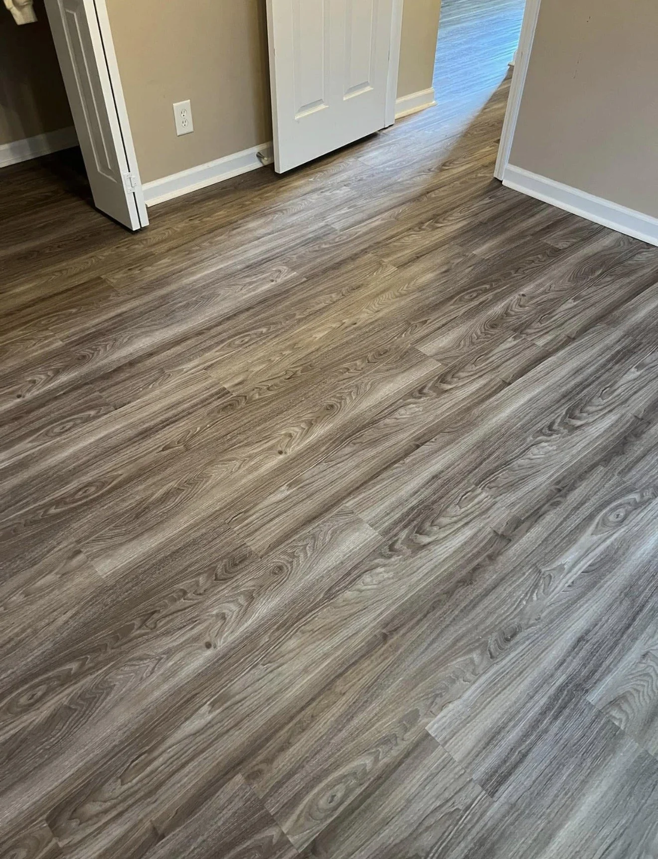 Wooden laminate flooring in a room with beige walls, white baseboards, and a partially open white door.
