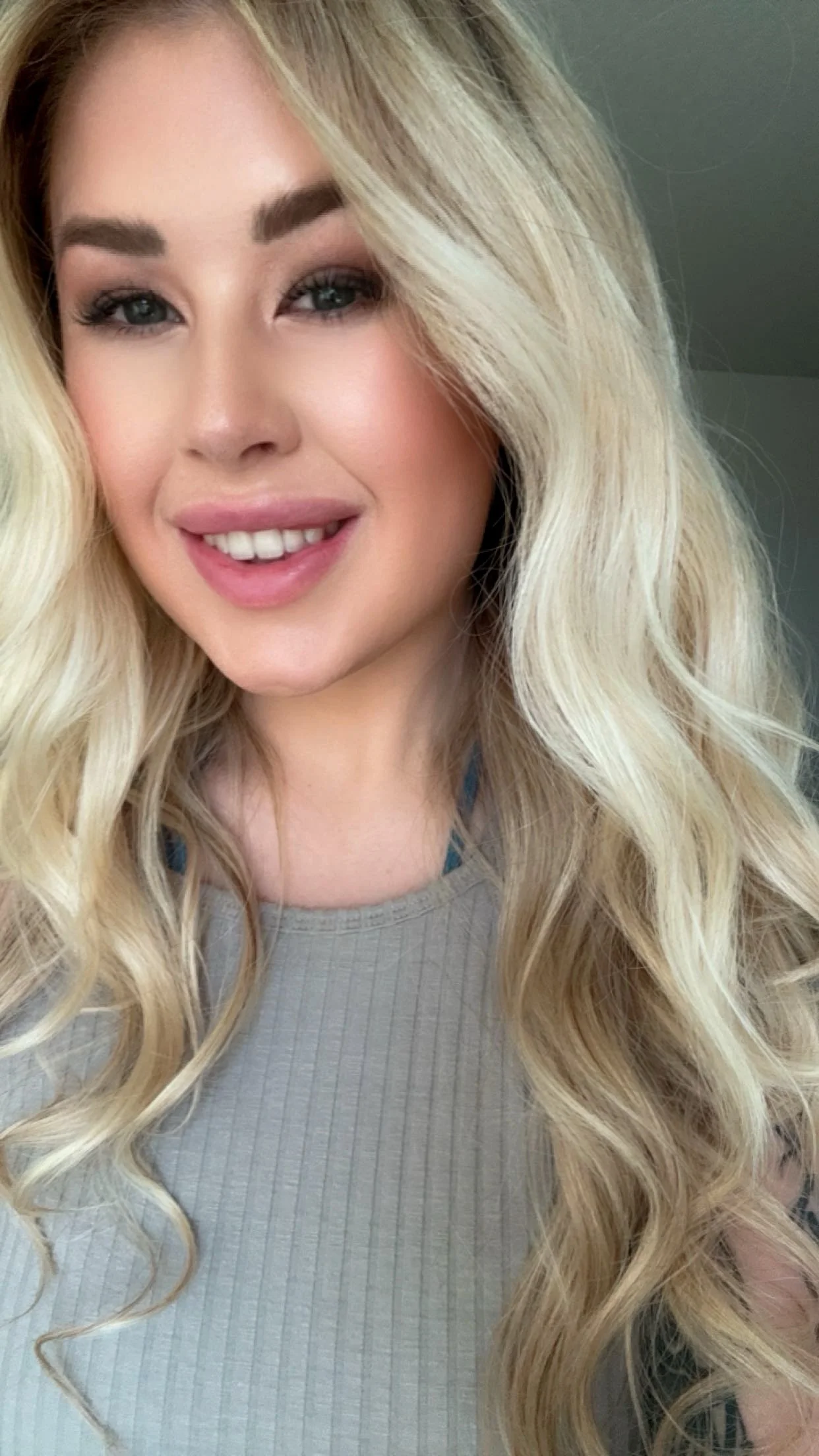 A woman with long, blonde curly hair smiling at the camera.