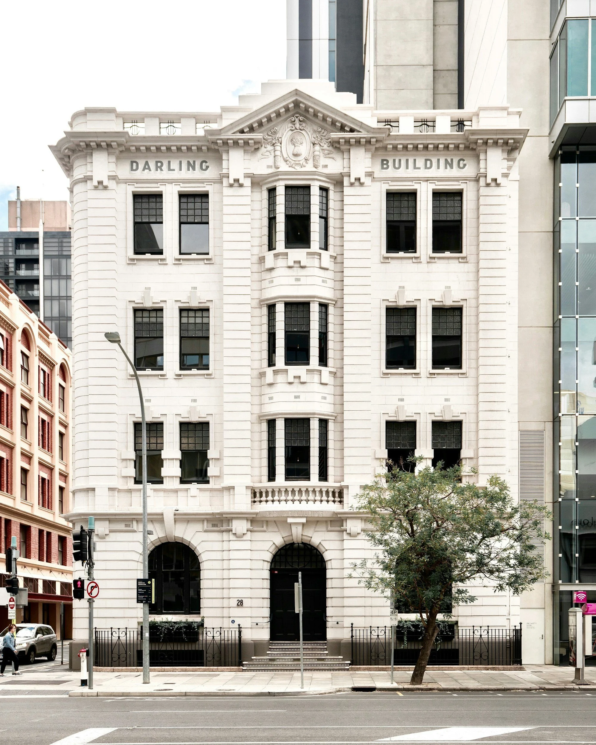 White historic multi-story building with decorative architecture, labeled 'Darling Building,' located on a city street with trees, cars, and pedestrians.