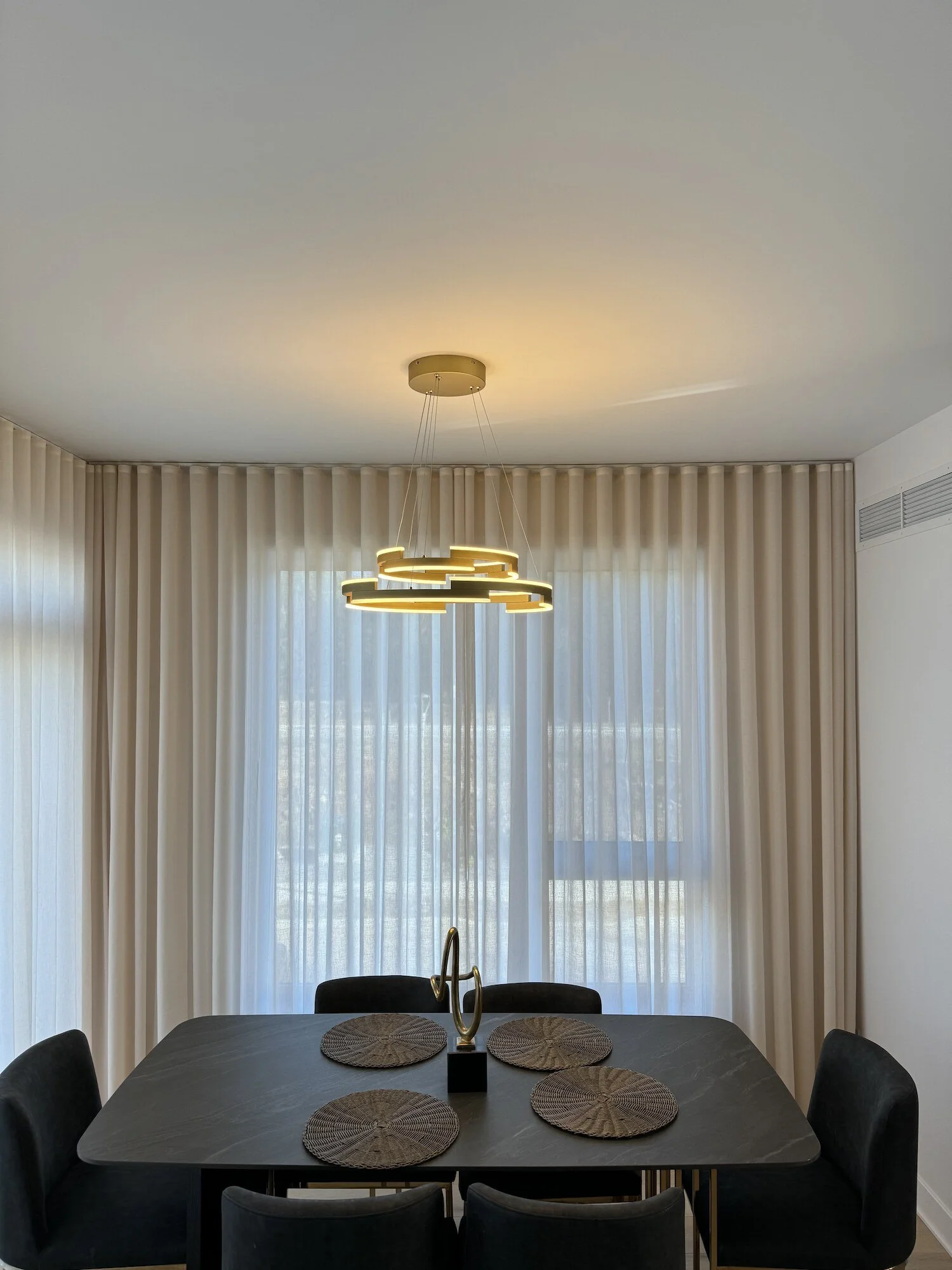 Sheer curtains and full-length drapery behind a dining table and gold chandelier