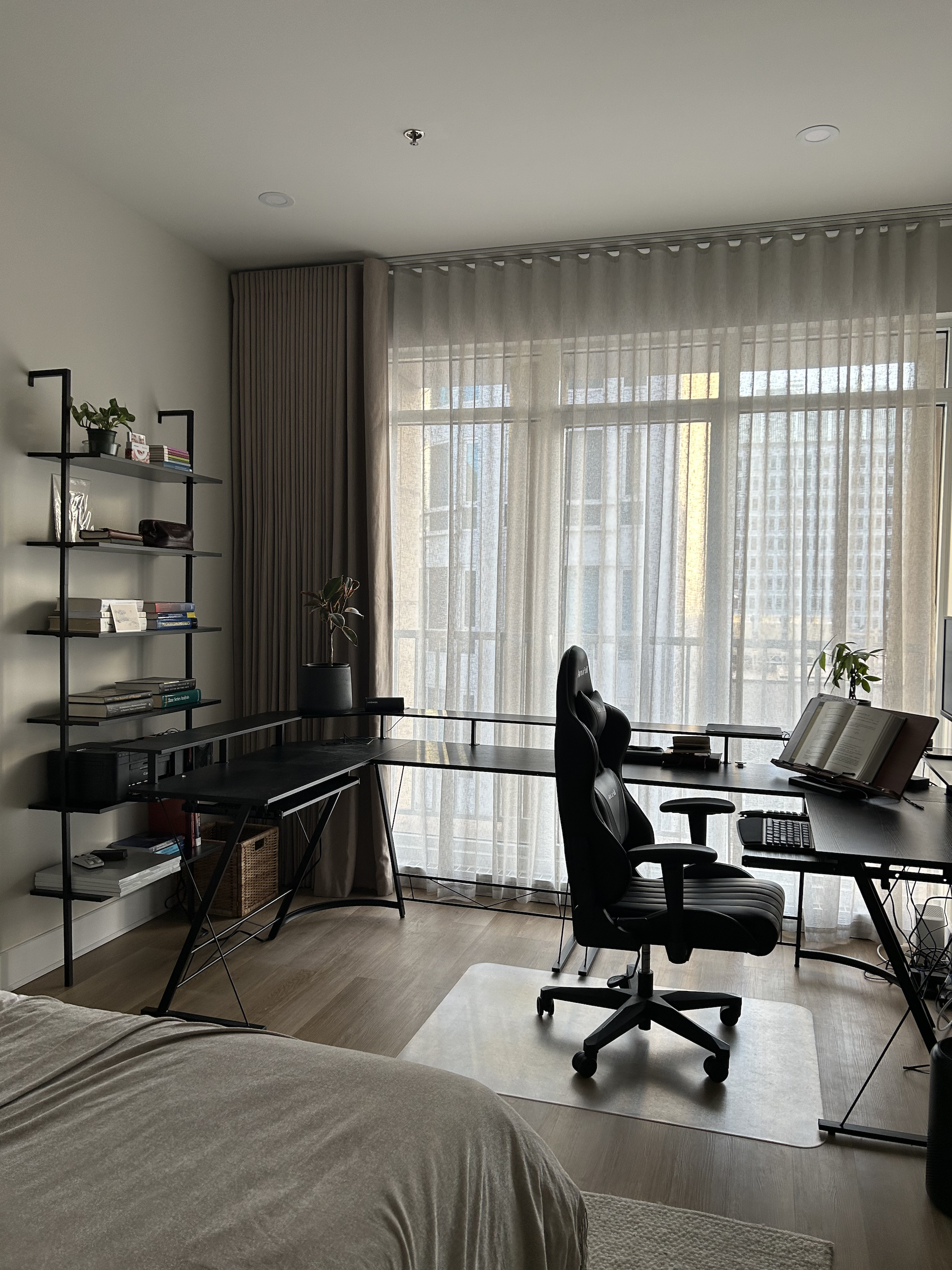 Modern home office with a large window, black desk, window shelf, office chair, and bookshelf.