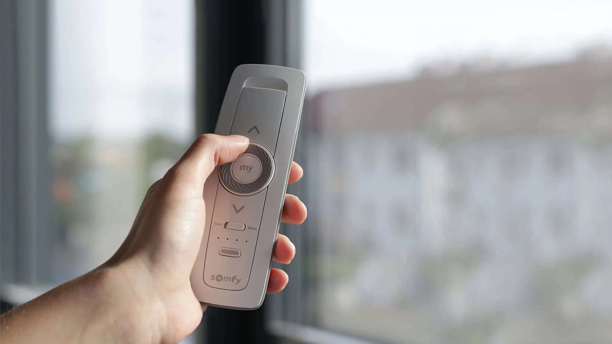 Hand holding a Somfy remote for motorized window shades