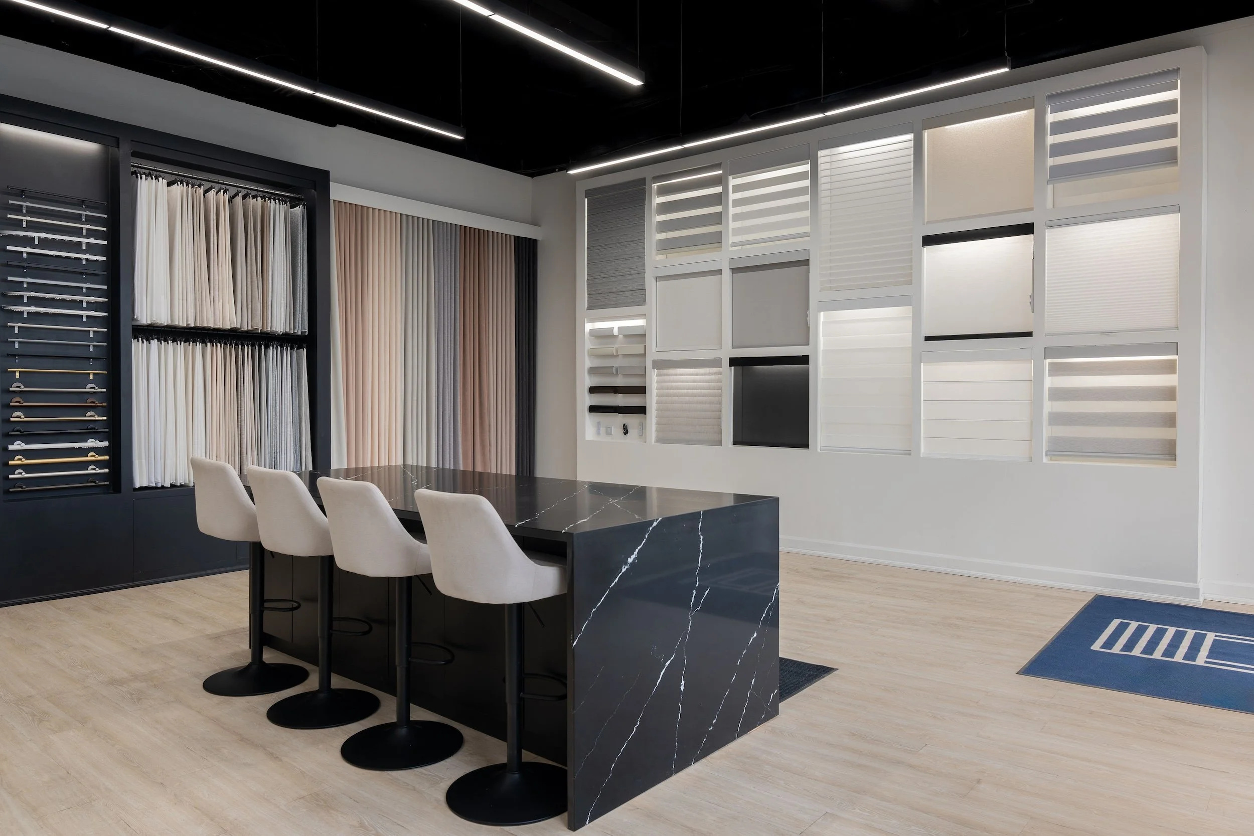 Showroom with fabric and window treatment samples, a black marble table, and beige chairs.