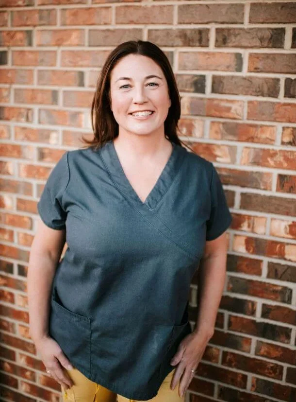 Smiling woman in navy scrubs standing against a brick wall.