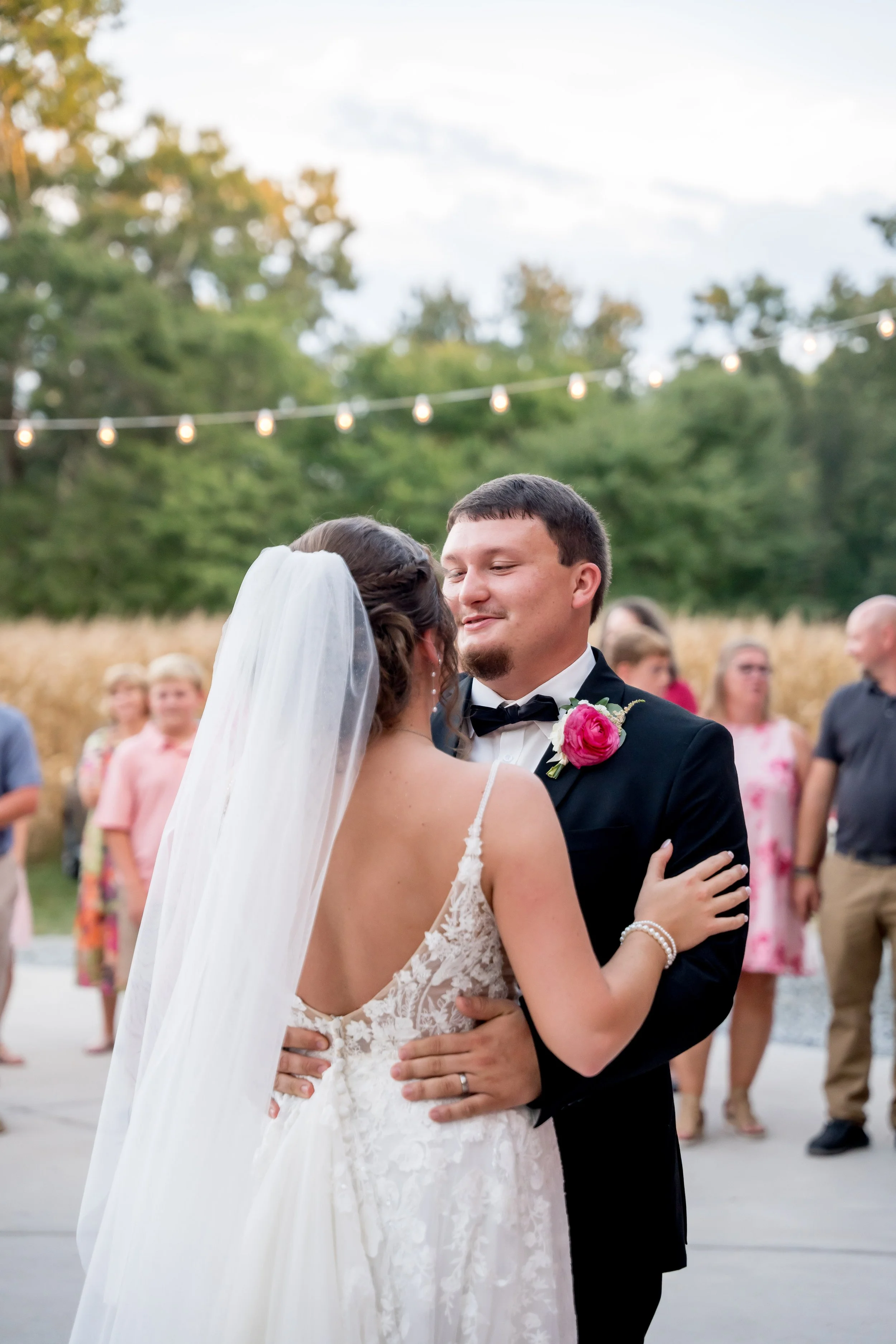 A bride and groom sharing their first dance during a wedding reception outdoors, surrounded by wedding guests.