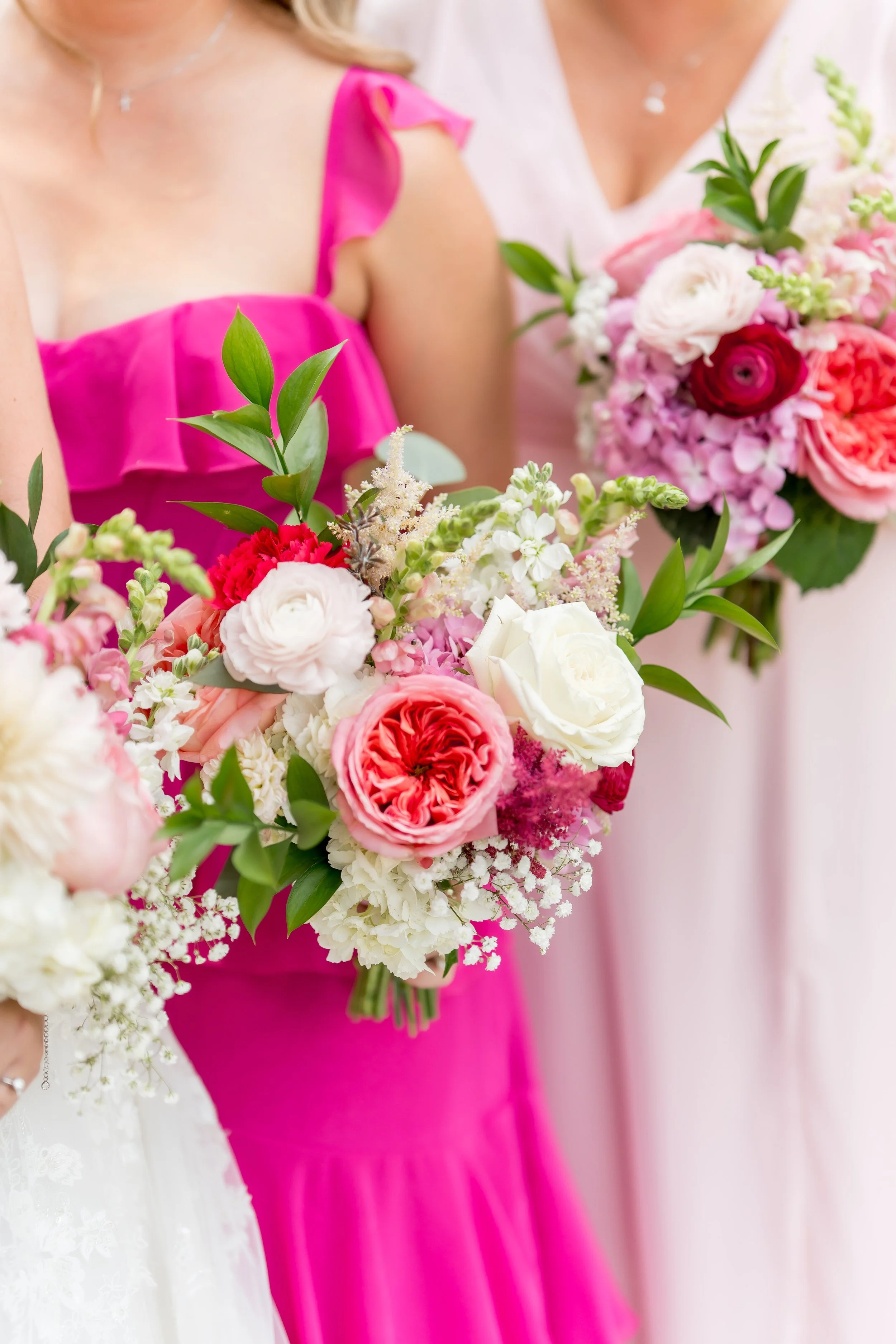 Close-up of women holding bouquets of pink, white, and red flowers at a celebration.