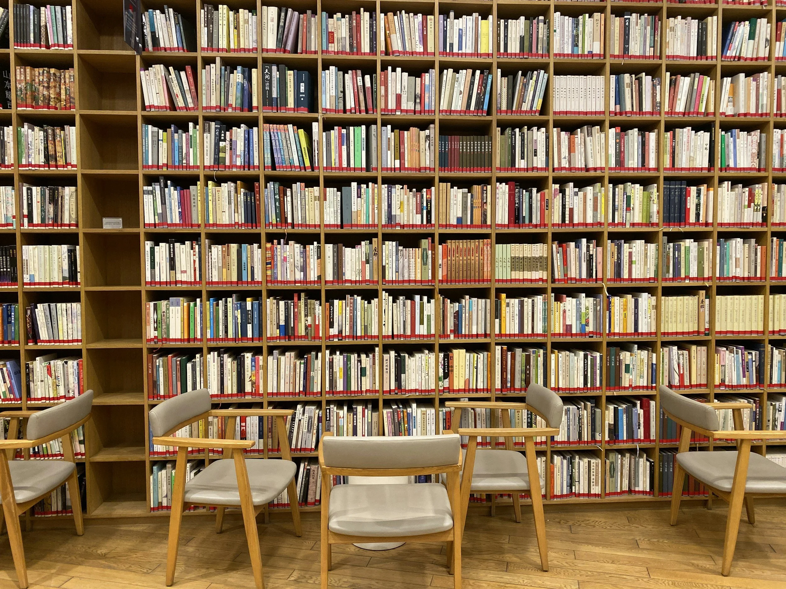A large shelf full of colorful books with three chairs positioned in front of it.
