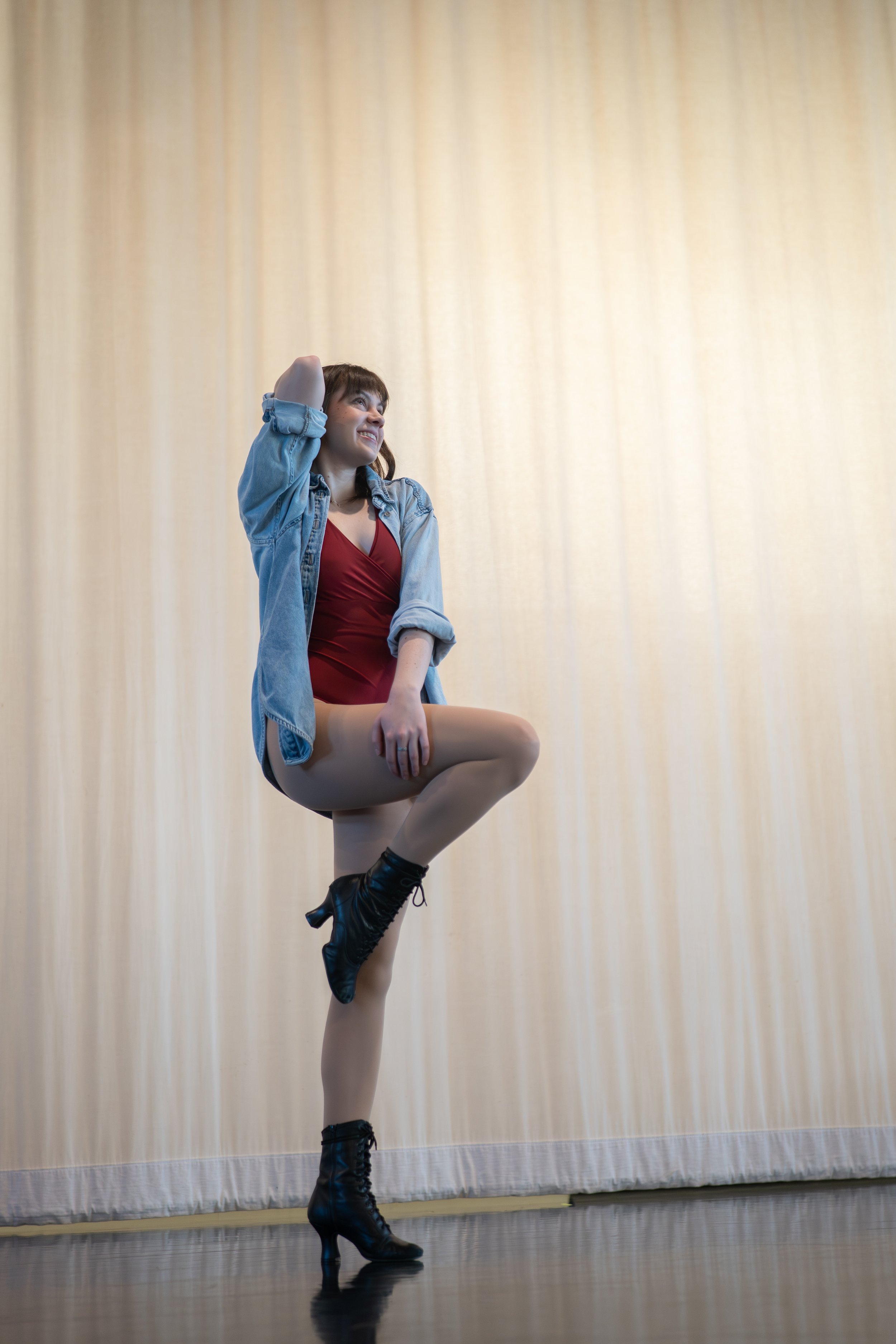 Gabriela Ayala Yarbrough smiling in a parallel passe wearing a red leotard and a denim shirt, looking off to the side