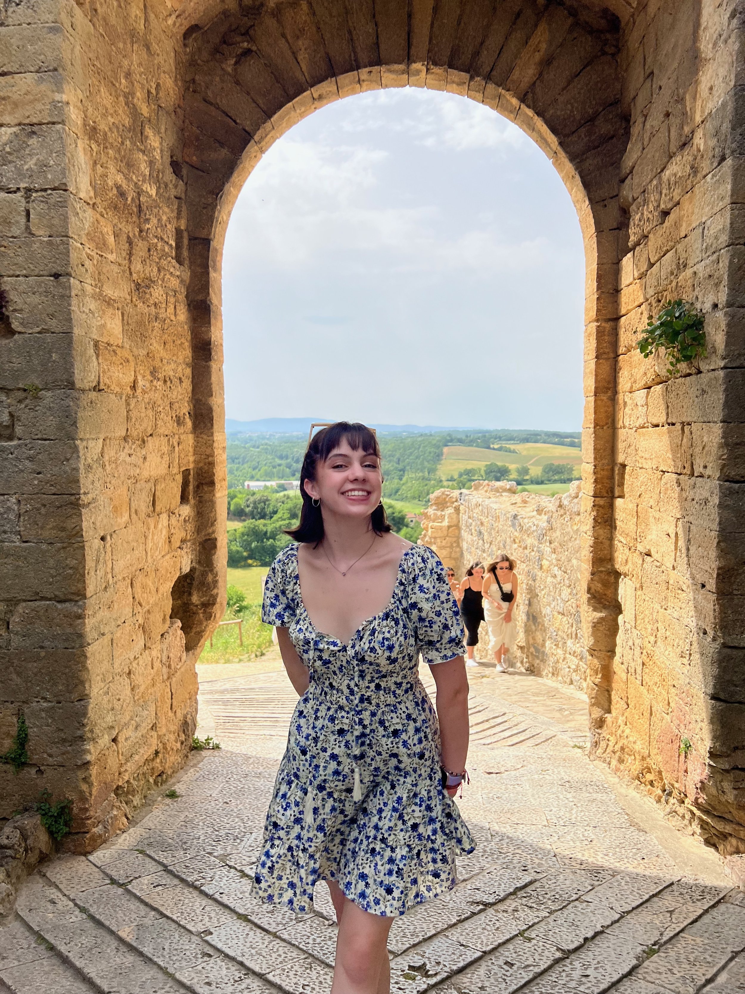 Gabriela Ayala Yarbrough smiling in a floral dress in front of an archway and greenery