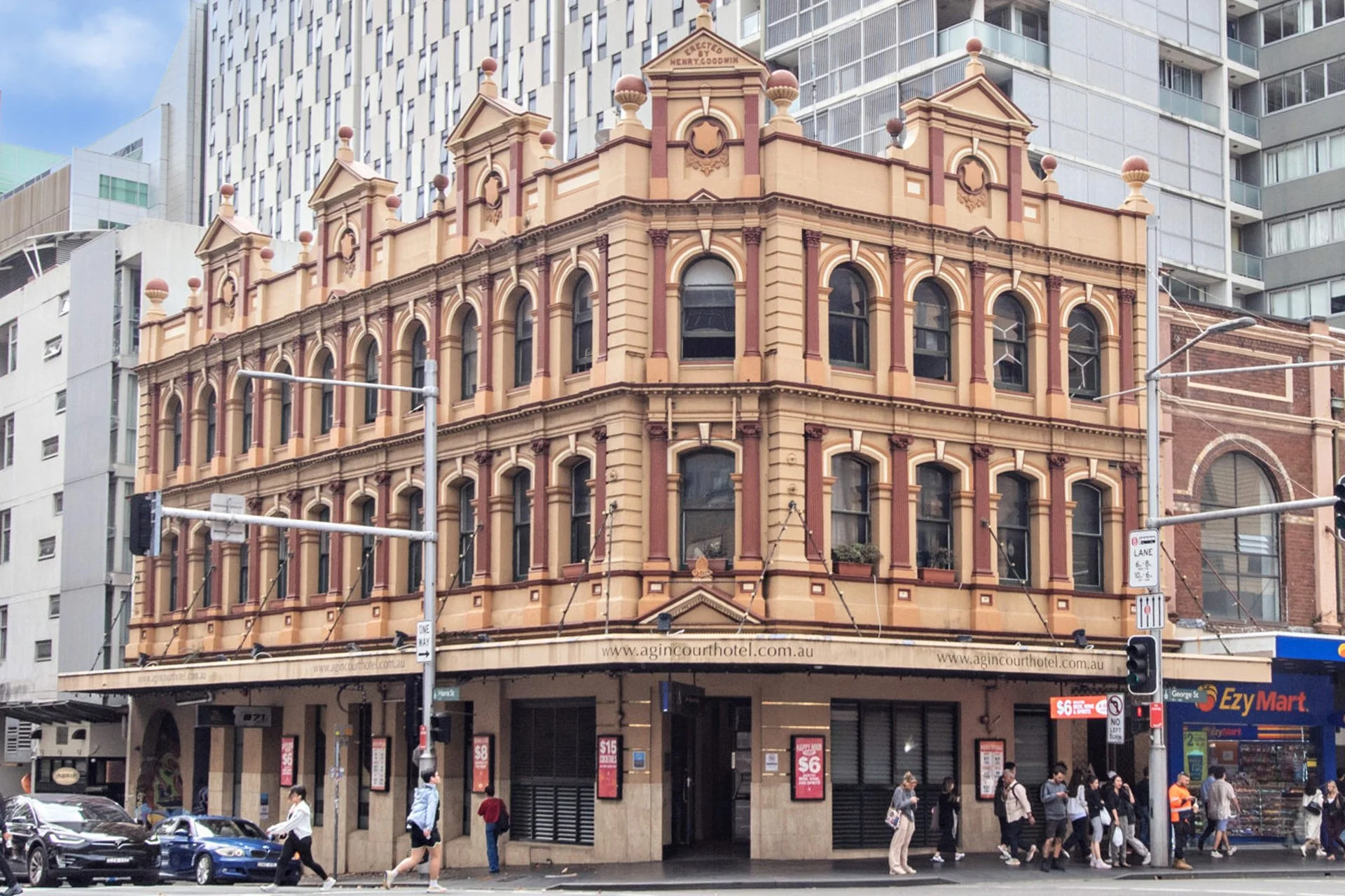 Historic four-story building with decorative architectural details, located on a busy city street with people walking and cars parked in front.