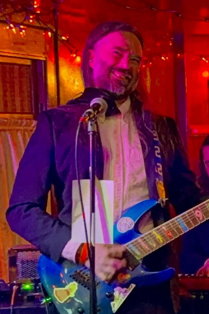 Glenn Smith in a suit playing a blue guitar