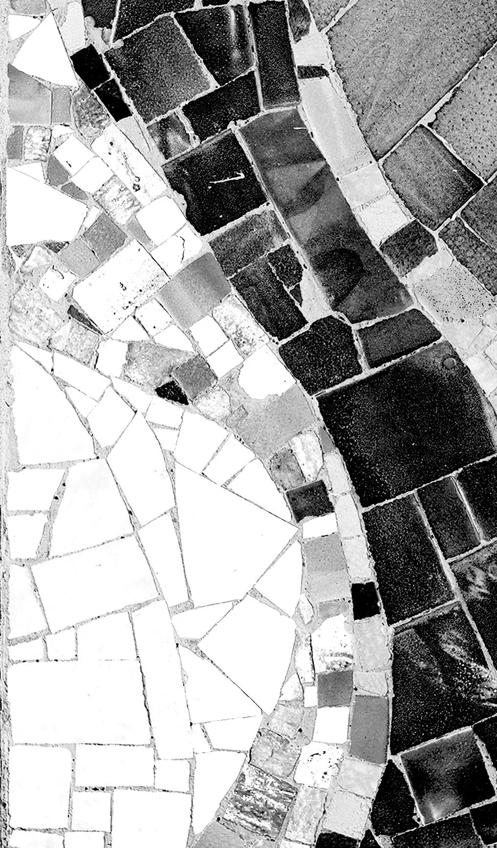 Close-up view of a mosaic tile floor with a curved pattern, made of variously shaped tiles in black, gray, and white.