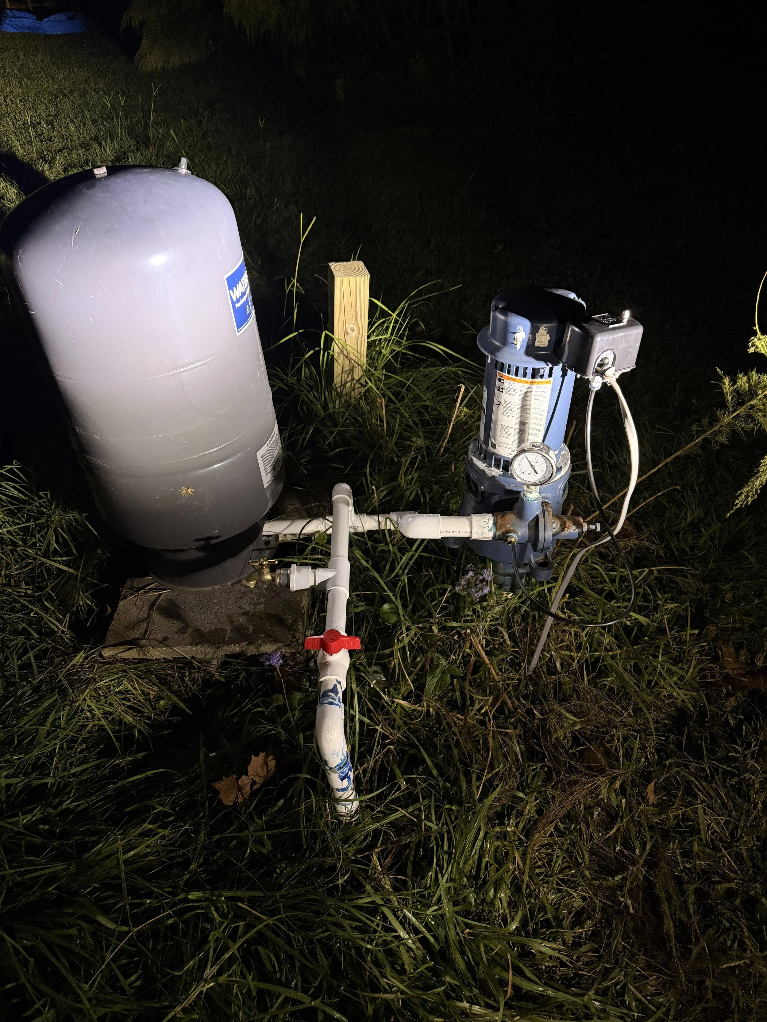 Outdoor water filtration or pump system on grass at night, with pipes, tanks, and gauges.