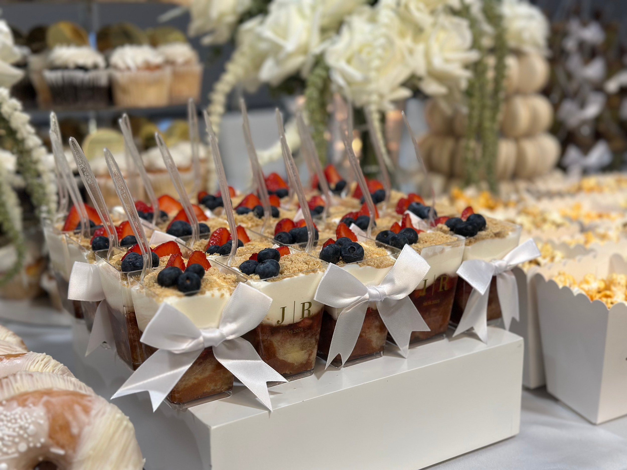 Dessert cups topped with strawberries, blueberries, and crumbled cookie on a white display stand, with floral decorations in the background.
