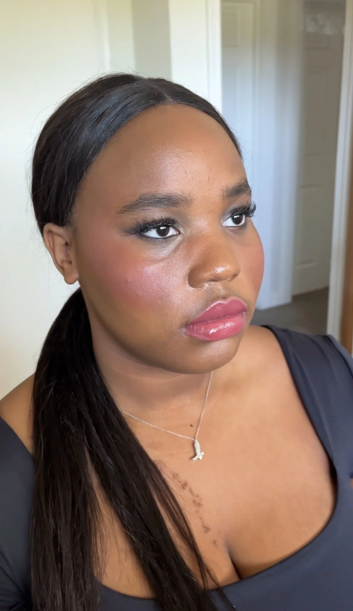Close-up of a woman with long dark hair, wearing a black top and a silver necklace, looking slightly to the side.