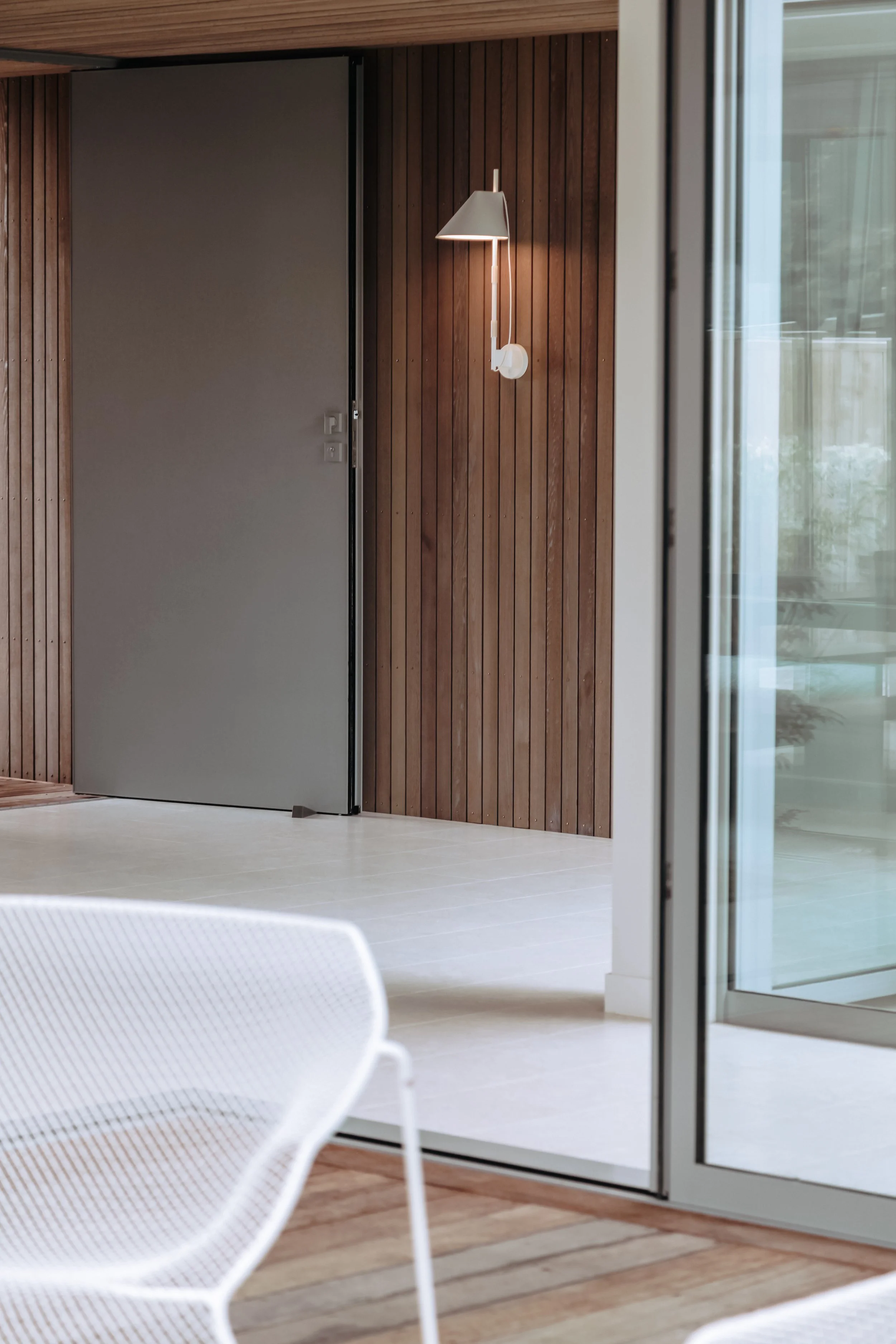 Modern interior with wooden wall paneling, sliding glass door, white chair, and wall-mounted lamp.