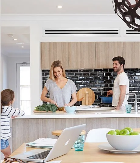 Family in a modern kitchen with a ducted split system air conditioning vent installed above cabinetry.