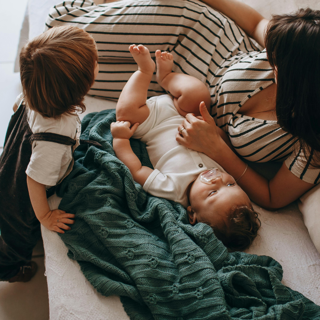 Mother lying with two young children on a bed in a family home