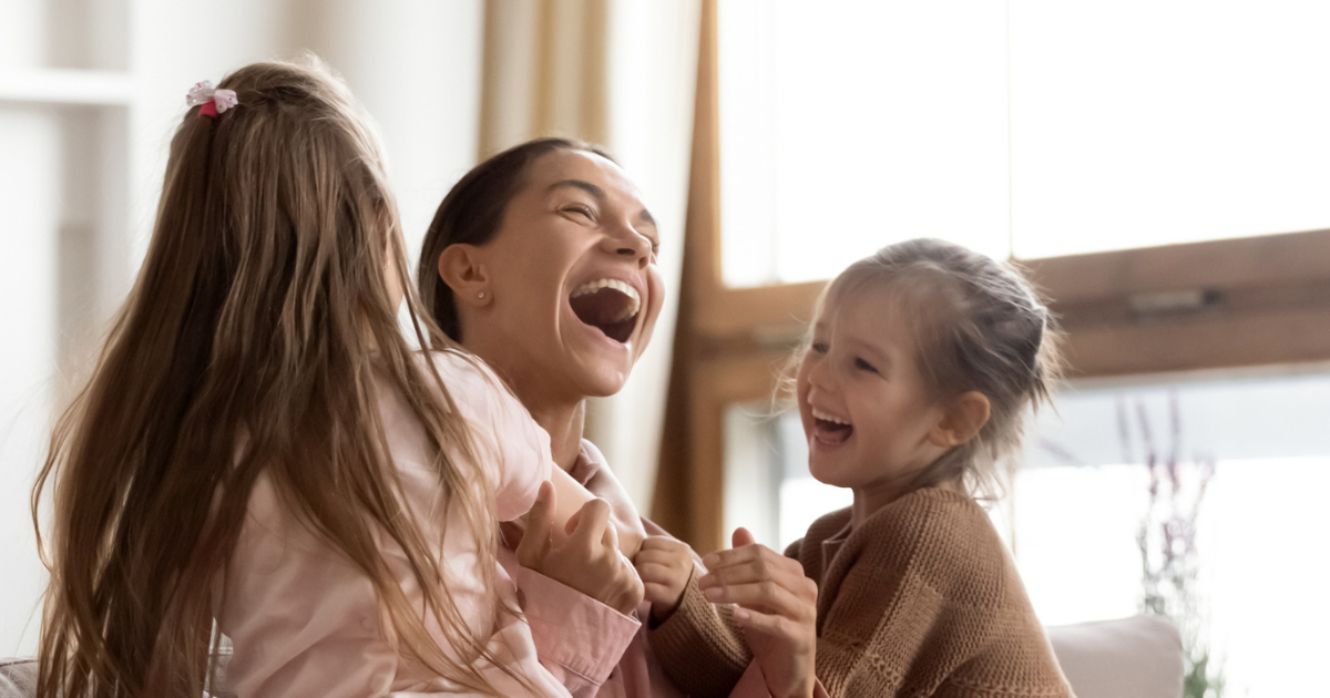 Three women smiling and laughing together indoors, engaging in a joyful moment.