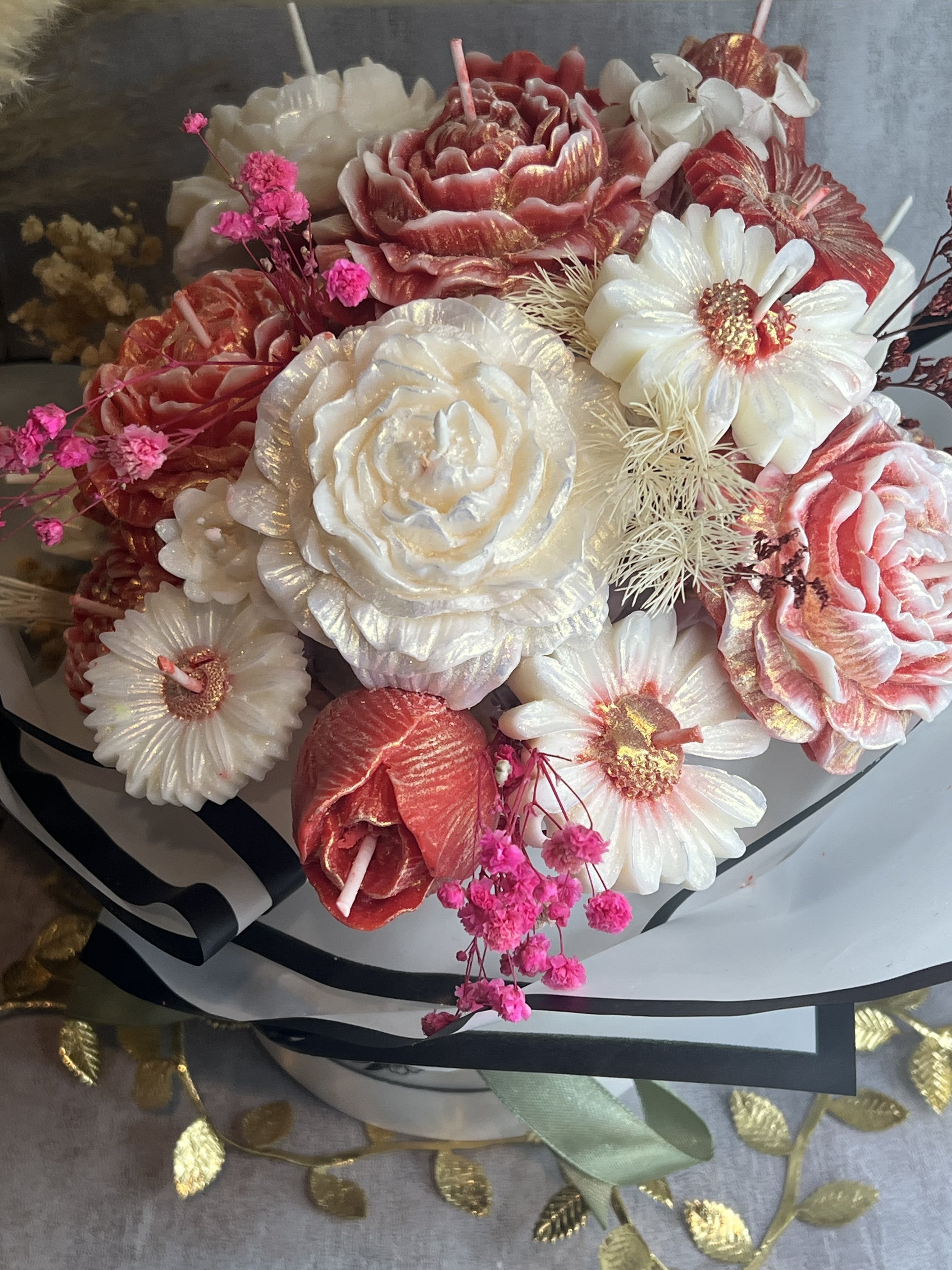 A bouquet of candles shaped like roses, tulips, and daisies with pink flowers and decorative foliage.