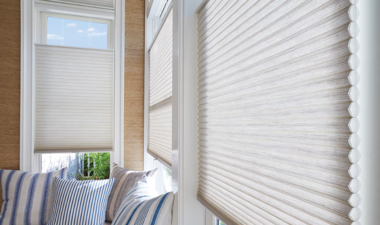Sunlight coming through white pleated window blinds in a bright room with a blue-striped cushion on a sofa.