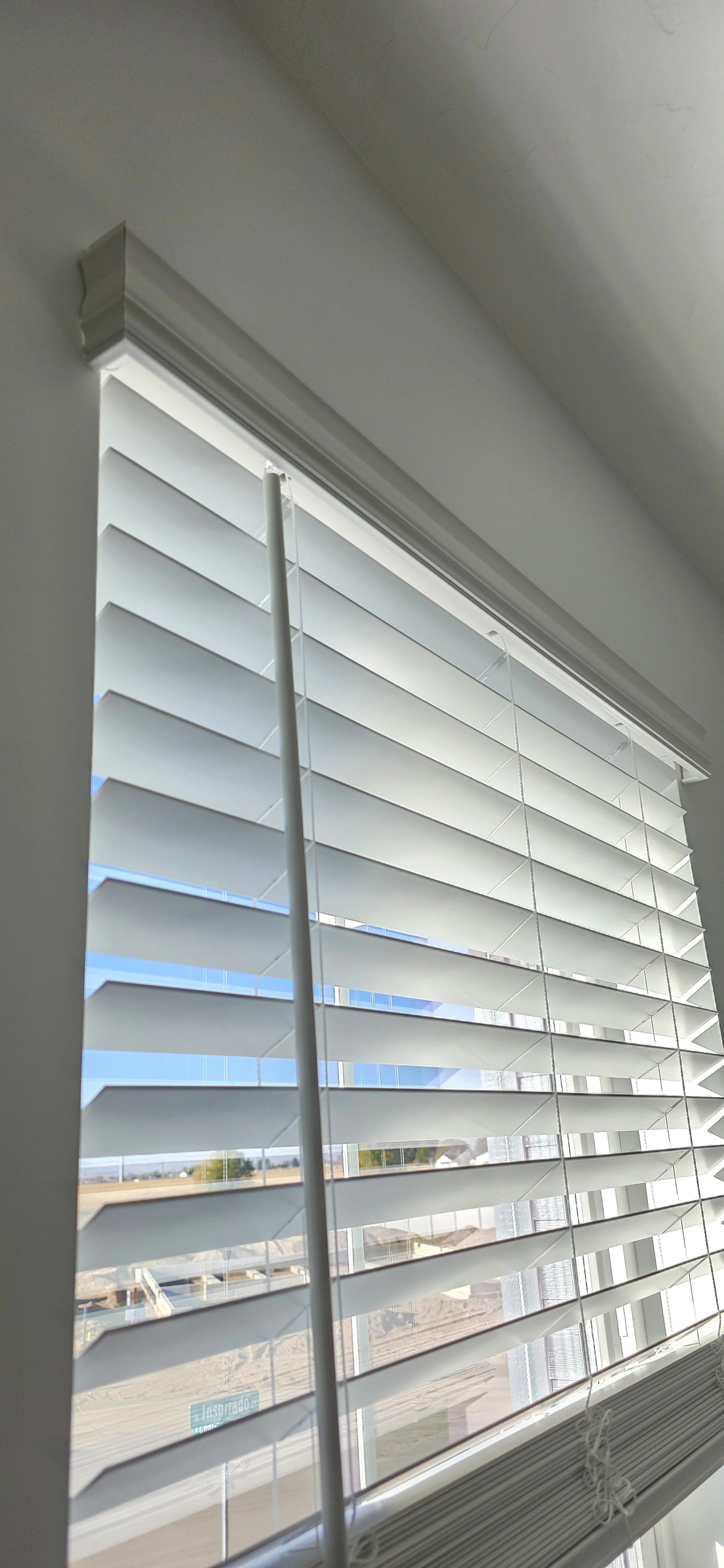A close-up of white horizontal window blinds partially open, allowing sunlight to stream into a room and revealing a view of a construction site outside through the clear glass window.