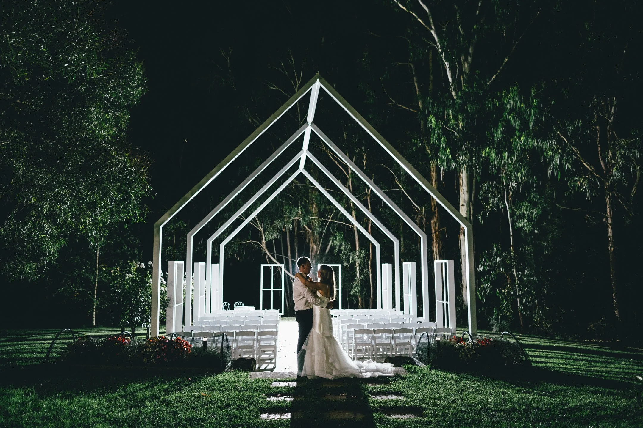 A couple dancing at their wedding under illuminated white geometric arches at night at Yarra Valley Estate