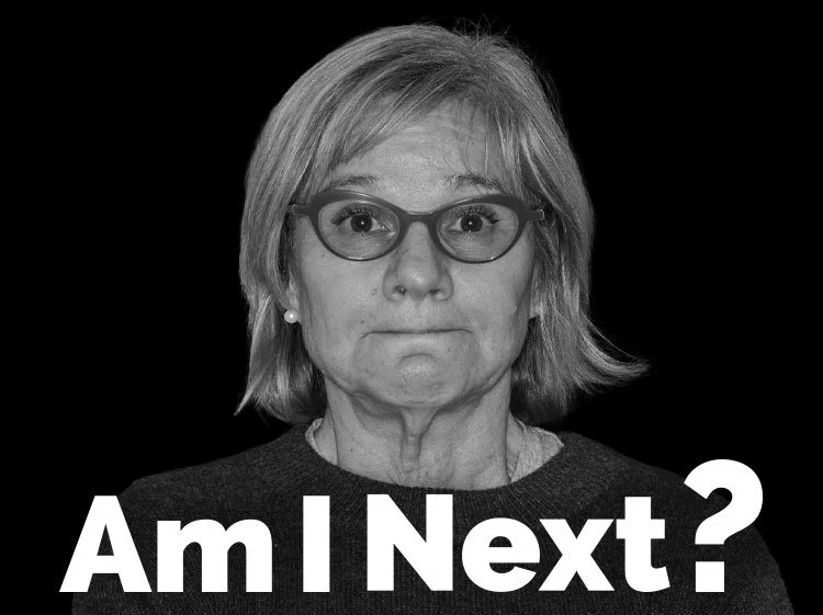Black and white photo of a middle-aged woman with glasses and shoulder-length hair, looking directly at the camera with a neutral expression, with the text "Am I Next?" in bold white letters at the bottom.