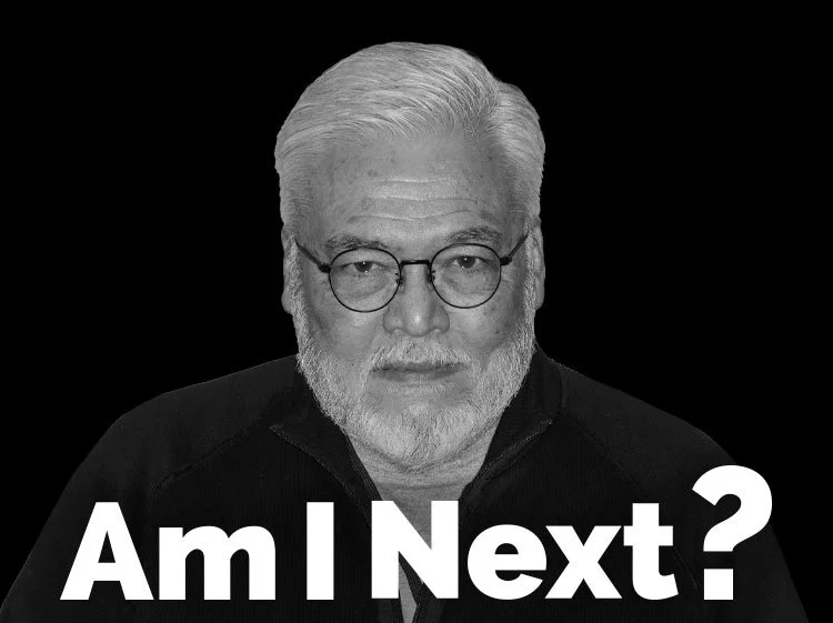 A black-and-white portrait of a man with white hair, beard, glasses, wearing a dark shirt, with the text "Am I Next?" in bold white letters at the bottom.