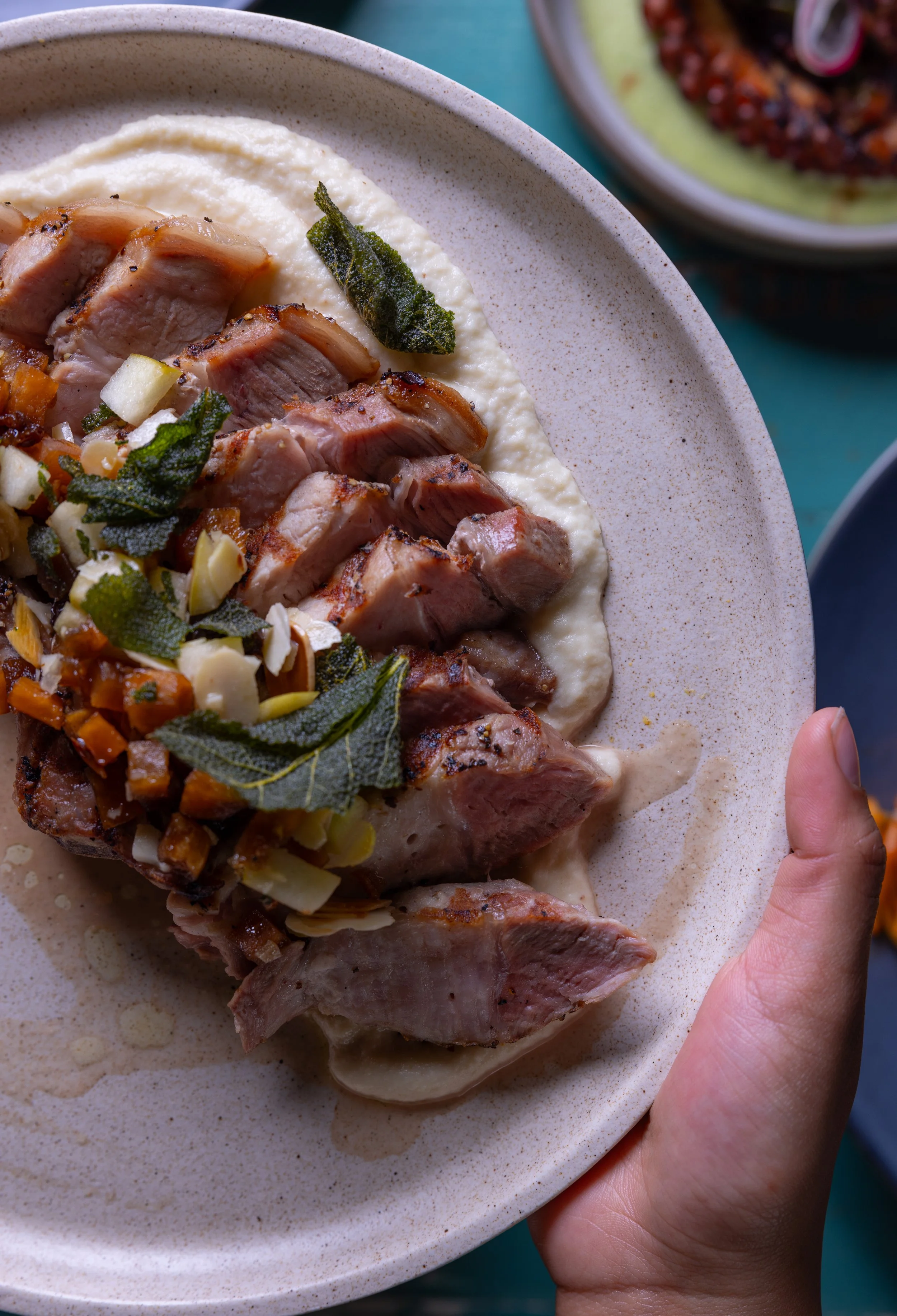A plate of roasted chicken served with mashed cauliflower, garnished with herbs and chopped almonds.