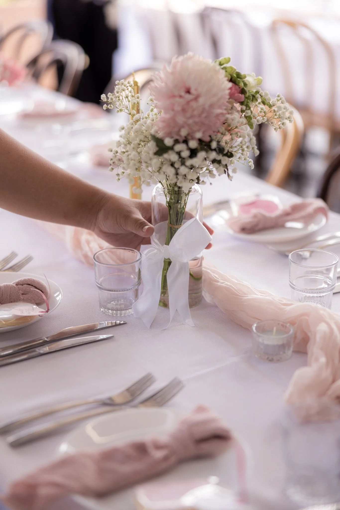 A person arranging a pink and white flower centerpiece on a dinner table decorated for a celebration.