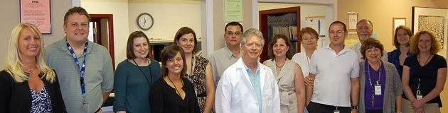 Group of 14 people standing together in an indoor setting, smiling at the camera.