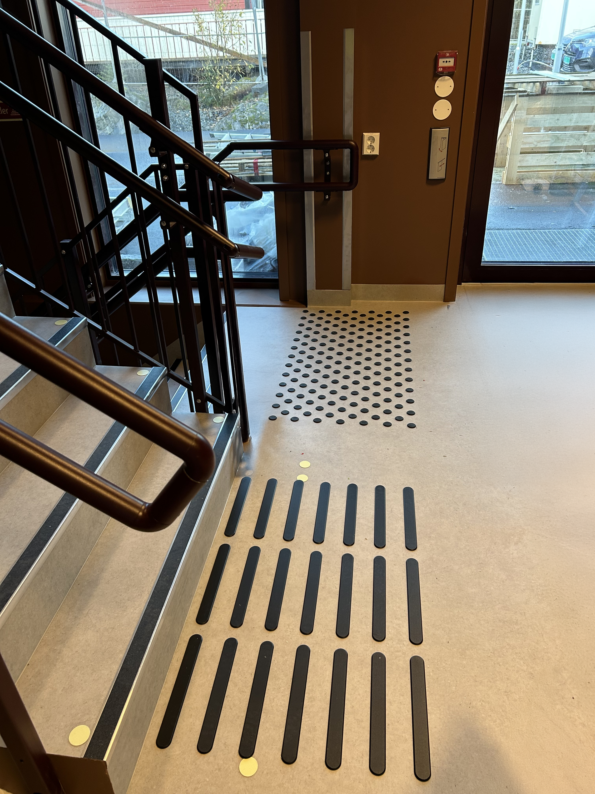 Innendørs trapp og glassdør med utsikt til parkering utenfor. Oppmerksomhetsfelt og farefelt.