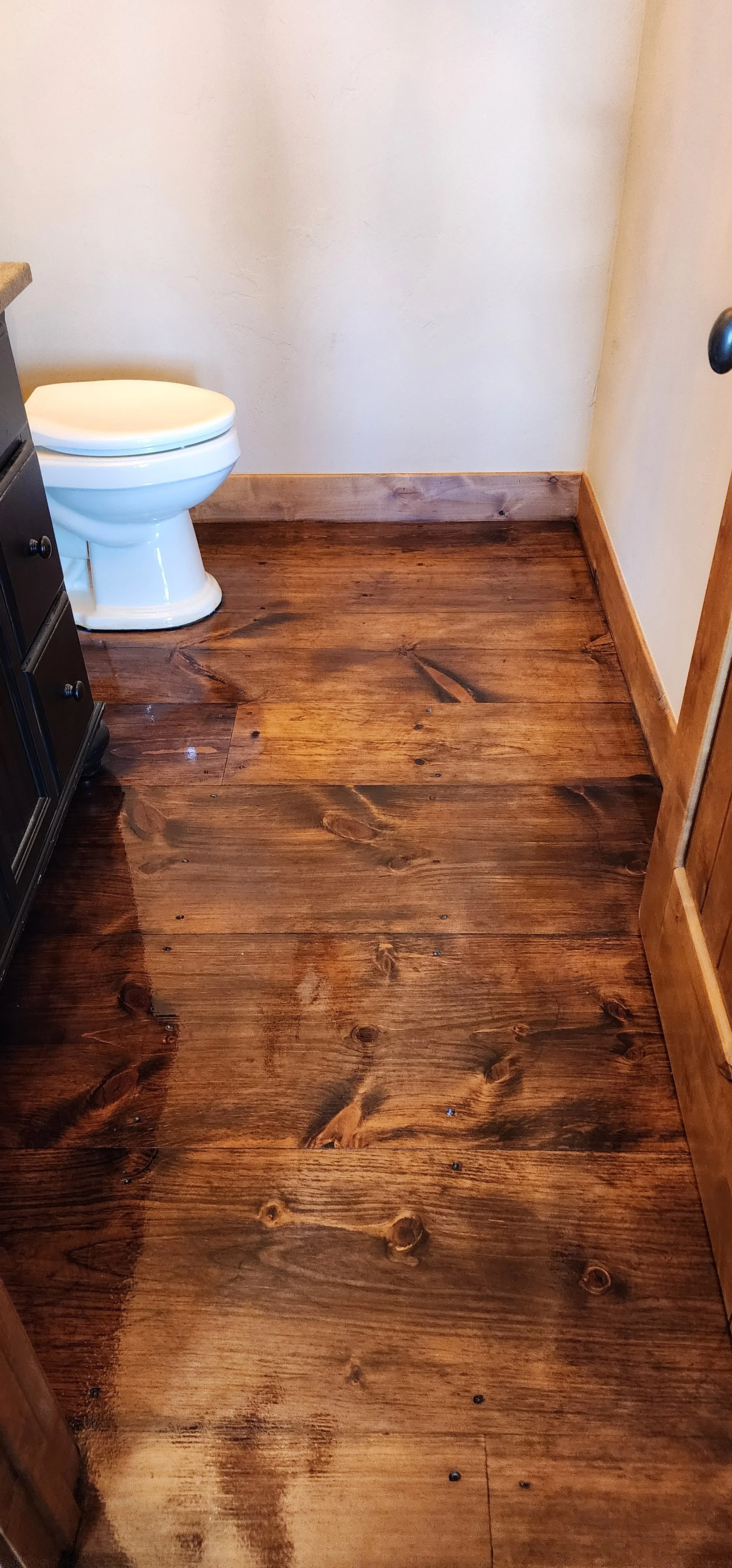Bathroom with wooden floor, toilet in the corner, and partial view of a cabinet on the left.