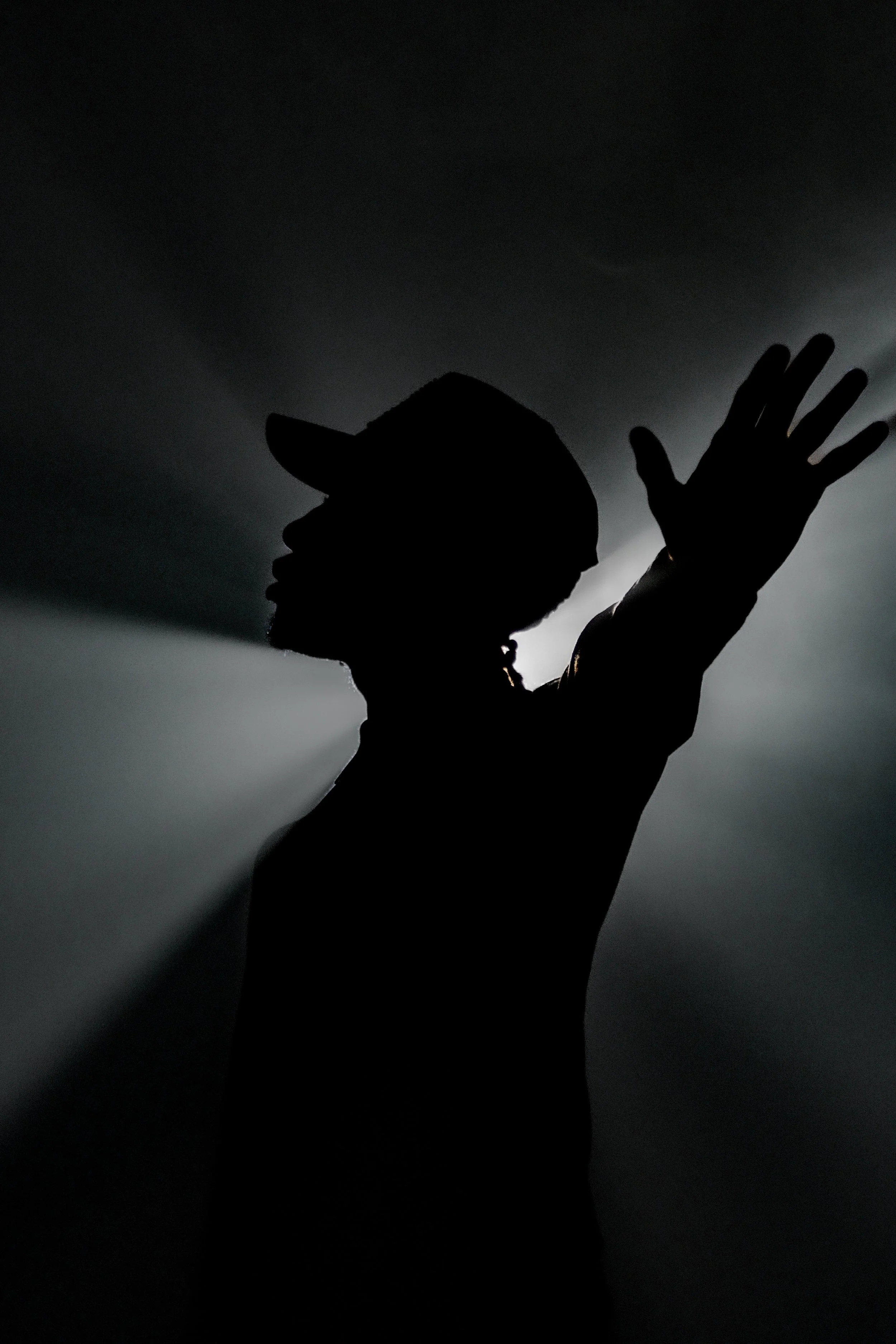 Silhouette of a man wearing a cap with one arm extended outward, backlit creating a dramatic shadow effect.