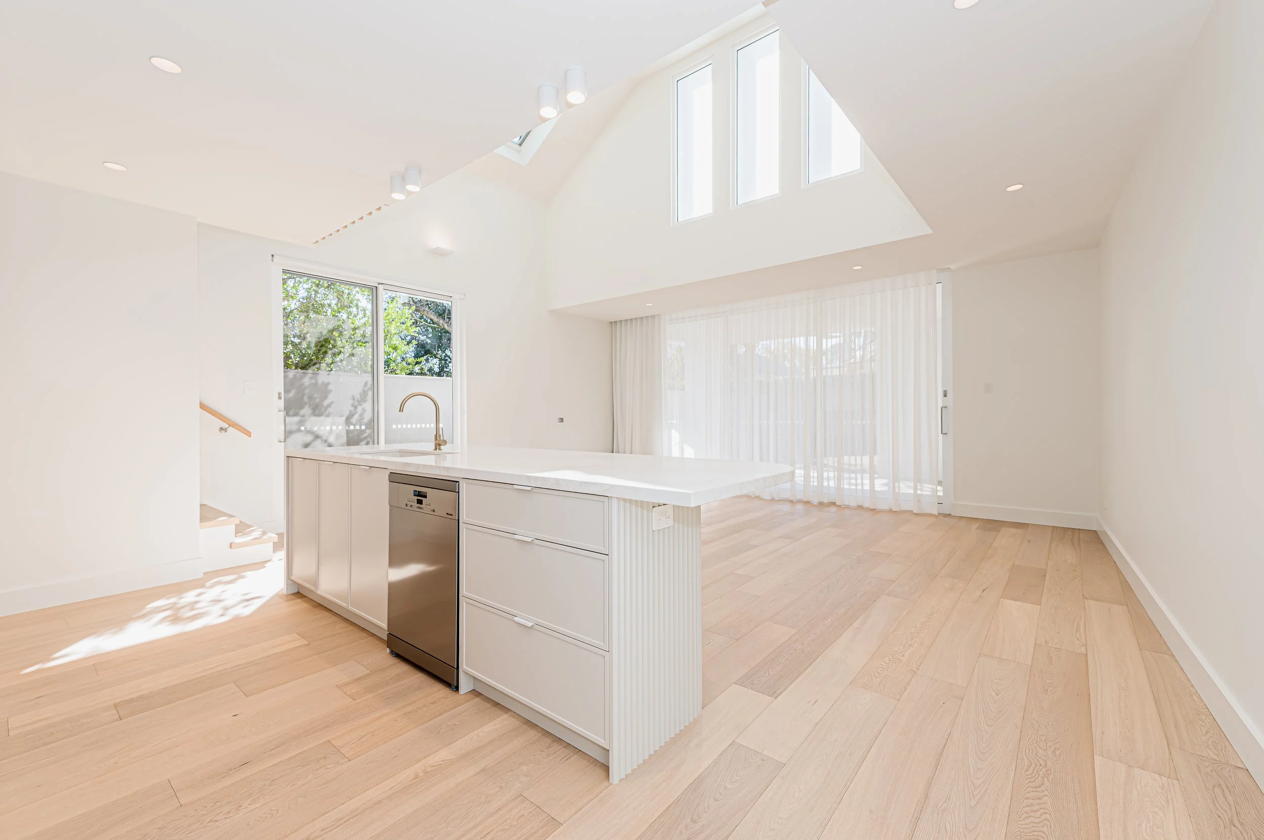 Simple white kitchen with light timber flooring and stone benchtops.