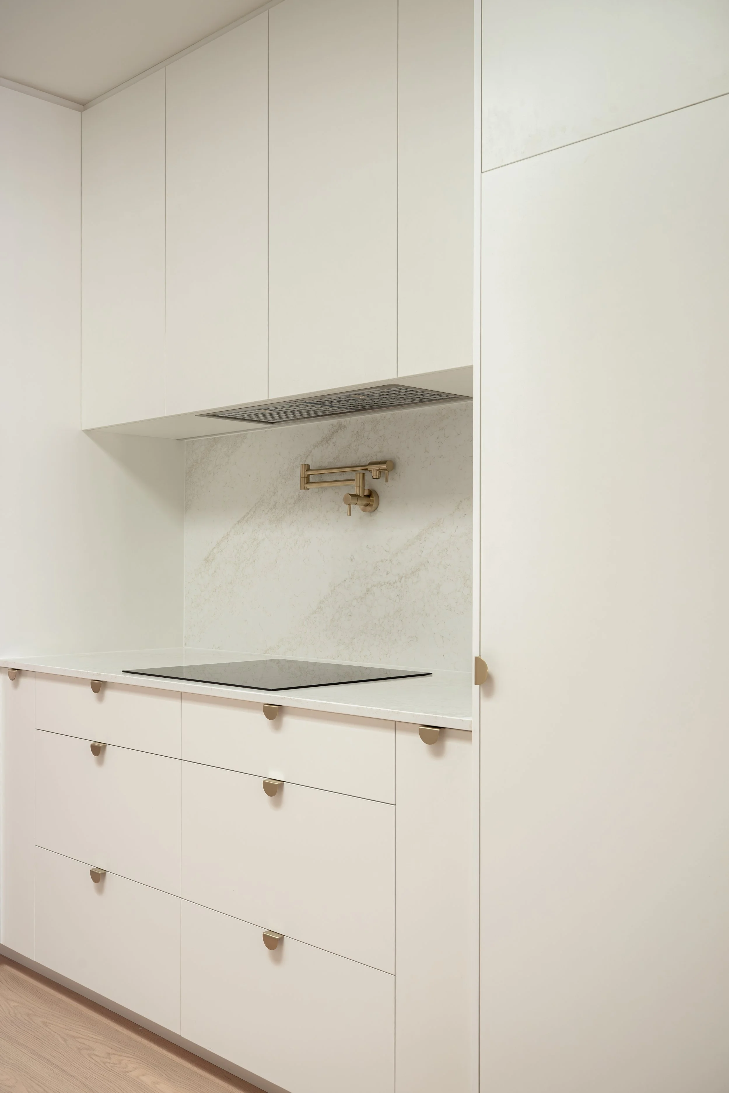 Classic white kitchen with brass handles, pot filler, and stone splashback. 