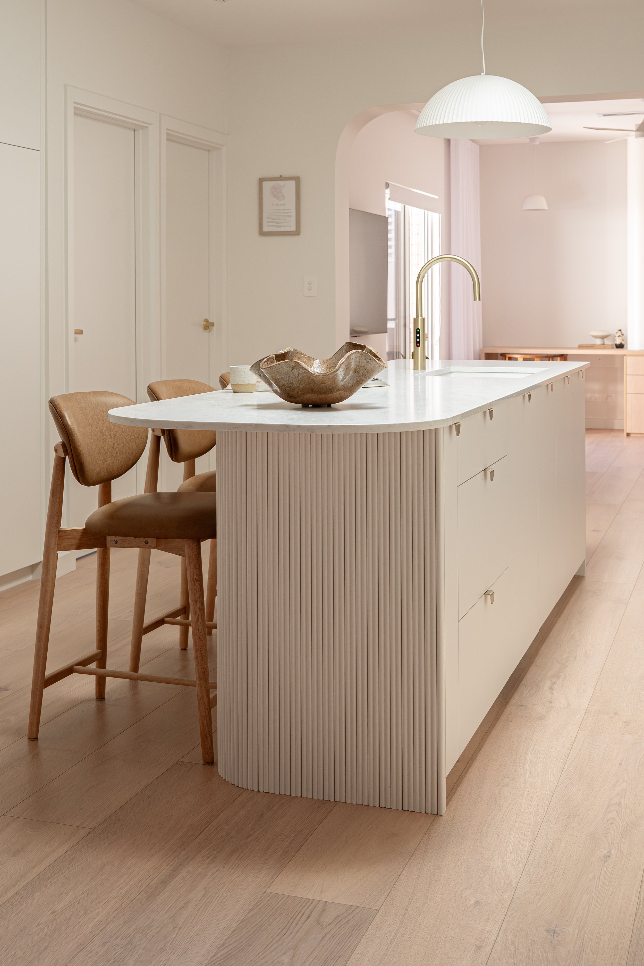 Classic white kitchen island with battoning, and tan stools. 