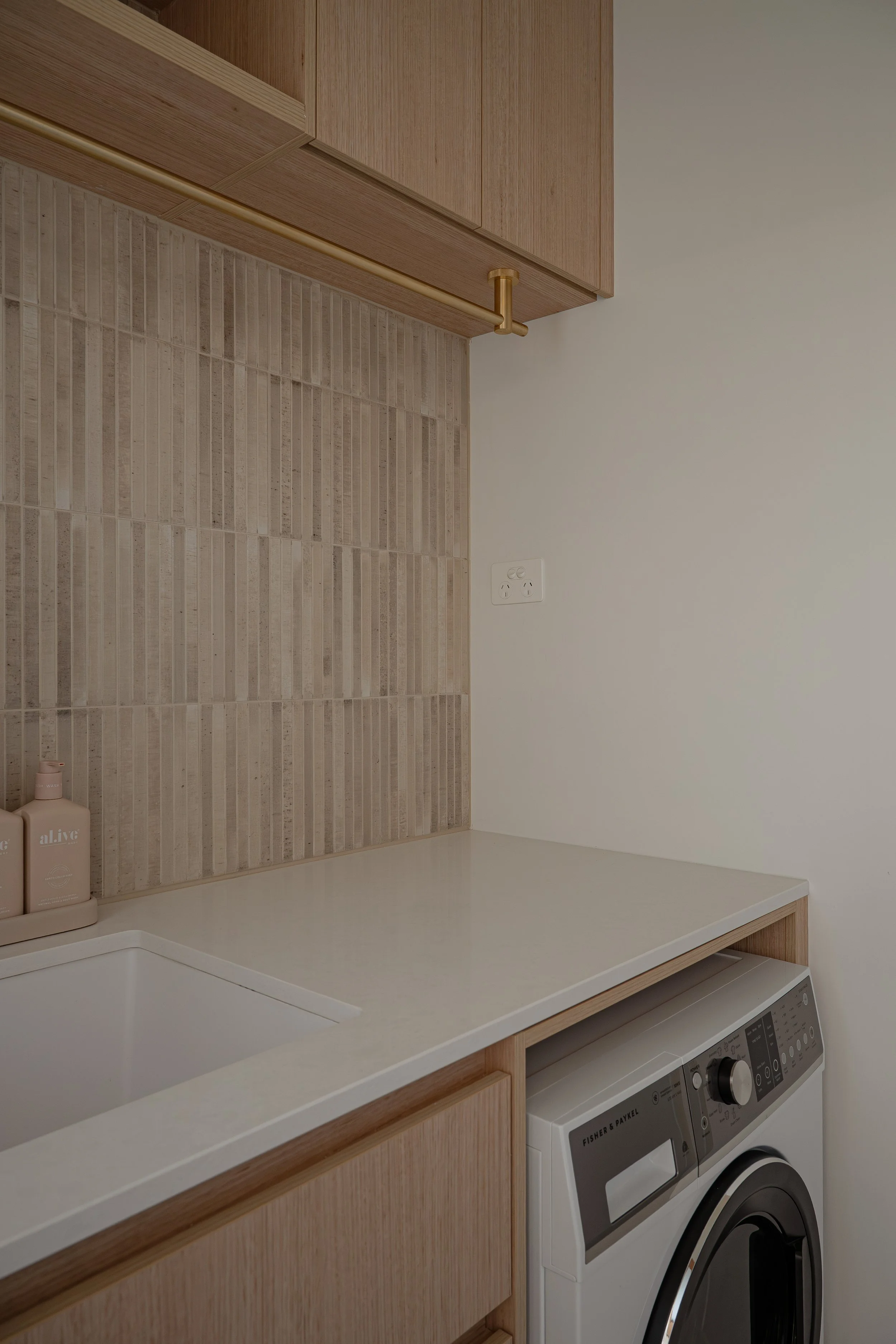 Timbergain laundry, featuring stone benchtop neutral tiles, and brass fixtures. 