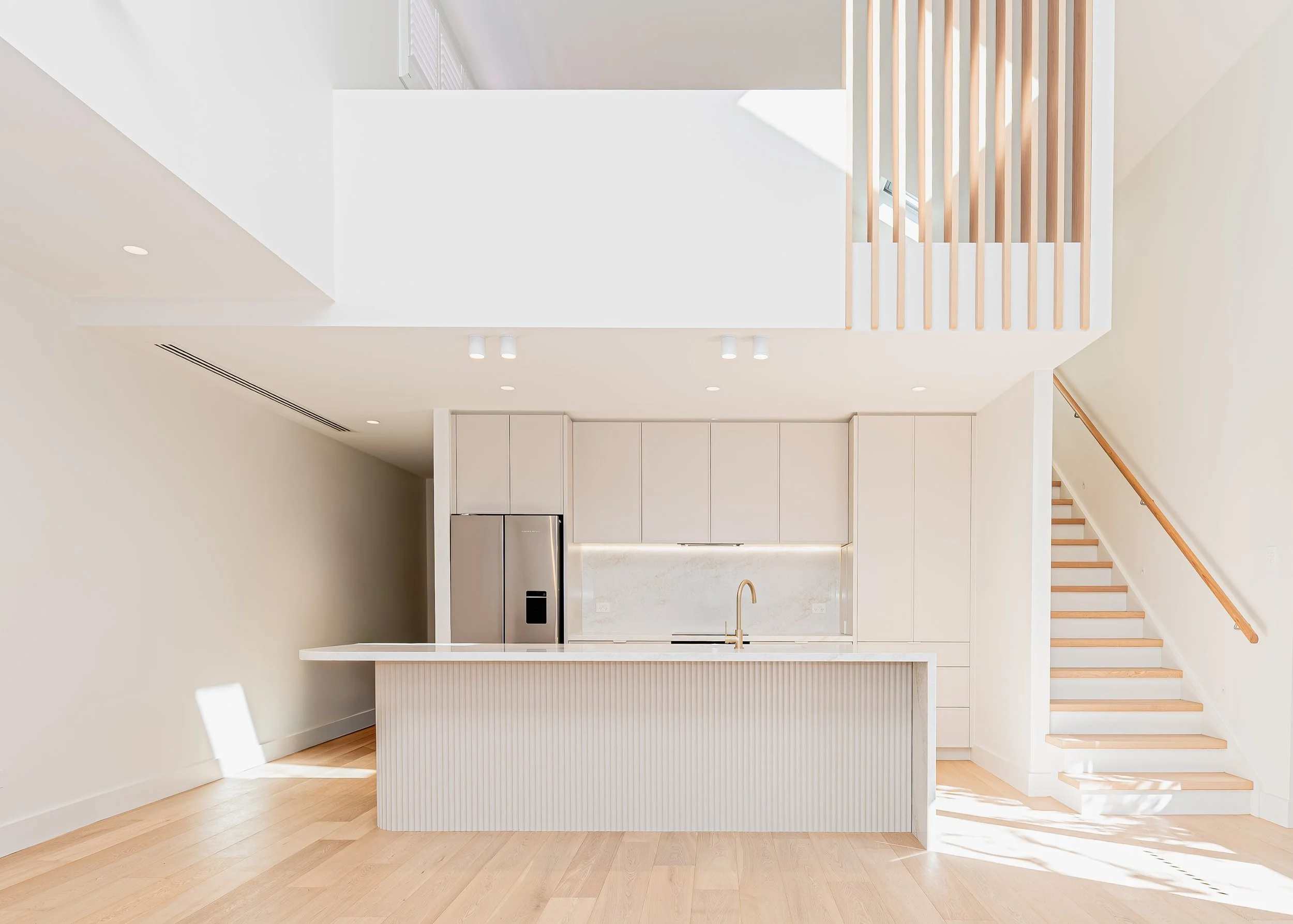 Simple white kitchen with light timber flooring and stone benchtops.