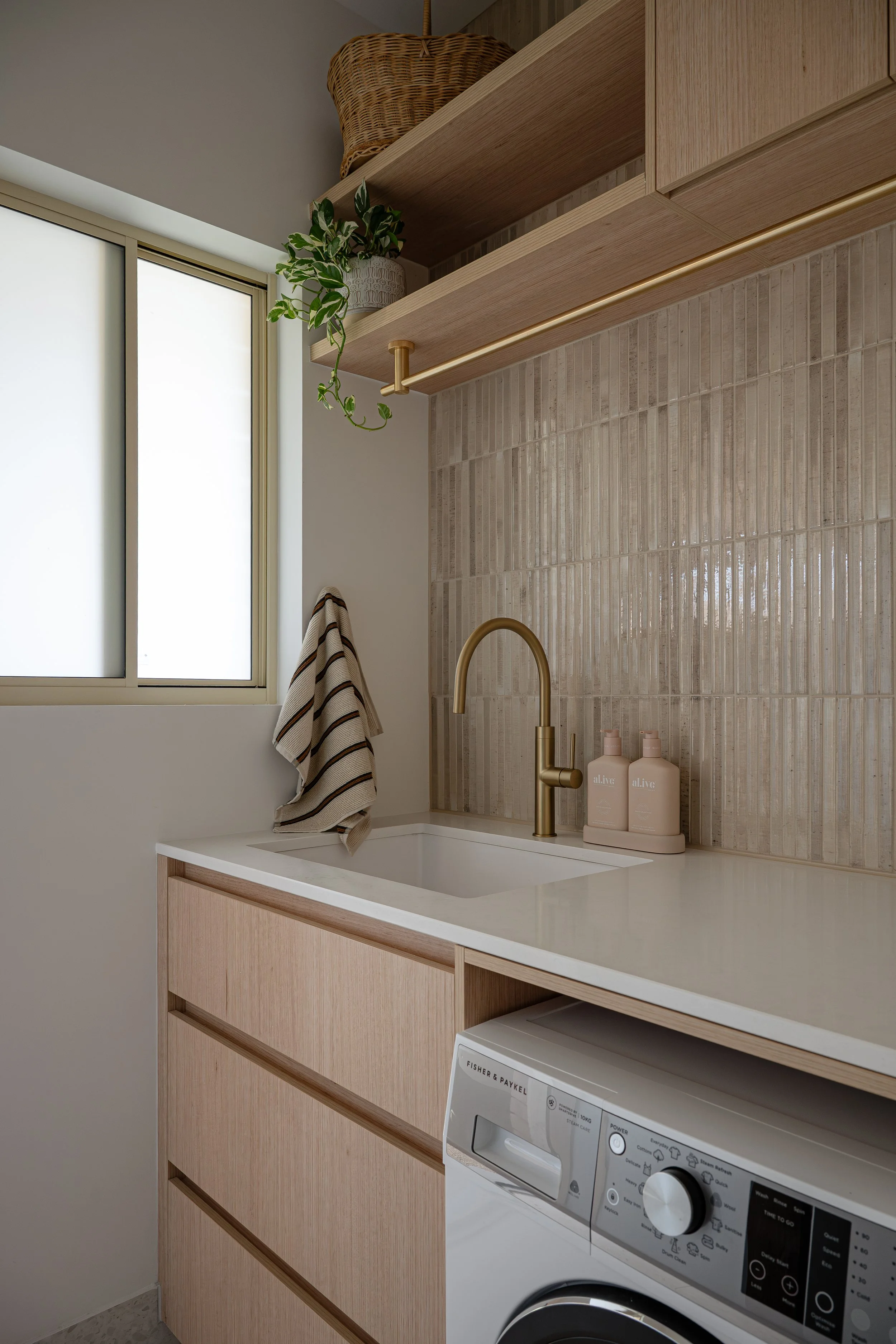 Timbergain laundry, featuring stone benchtop neutral tiles, and brass fixtures. 