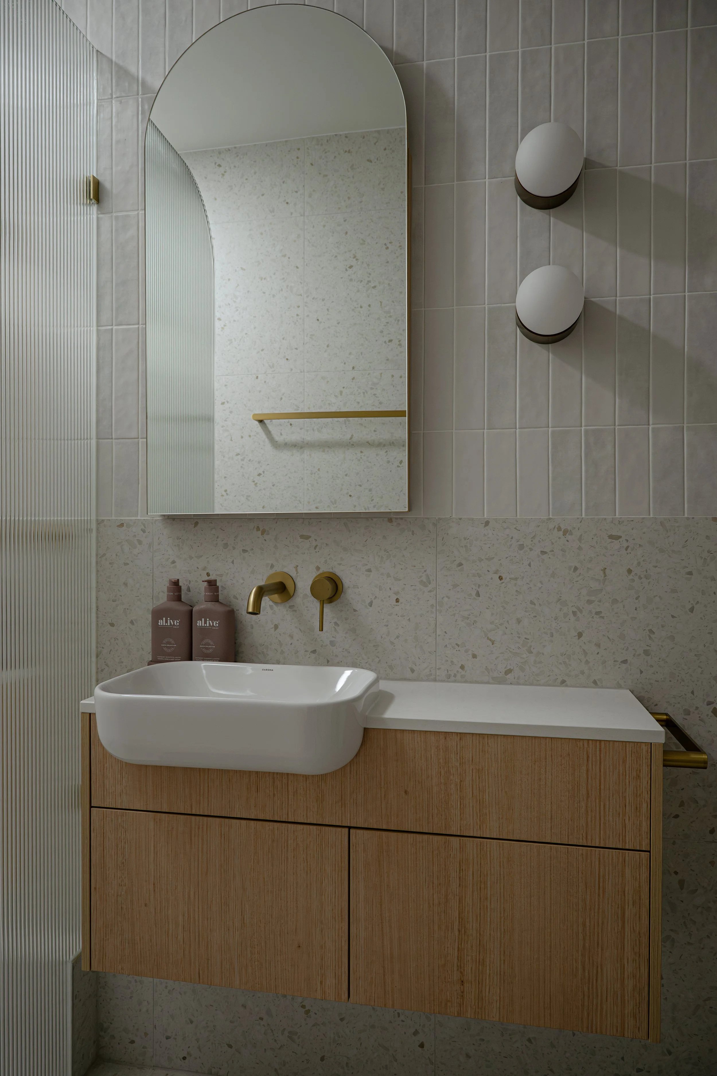 Timbergrain vanity with stone benchtop, in a neutral bathroom with multi tiles and feature wall lights. 