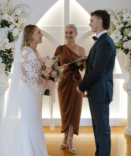 Bride and groom exchange vows during a wedding ceremony with officiant in a decorated indoor venue.