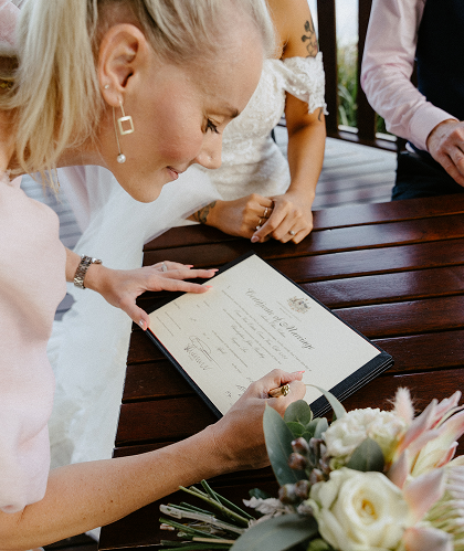 Bride signing a marriage certificate at a wedding ceremony with a bouquet of flowers nearby.