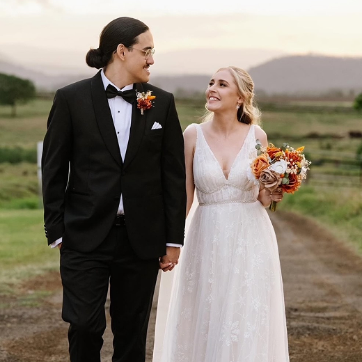 Bride and groom holding hands and smiling in a scenic outdoor setting during wedding.