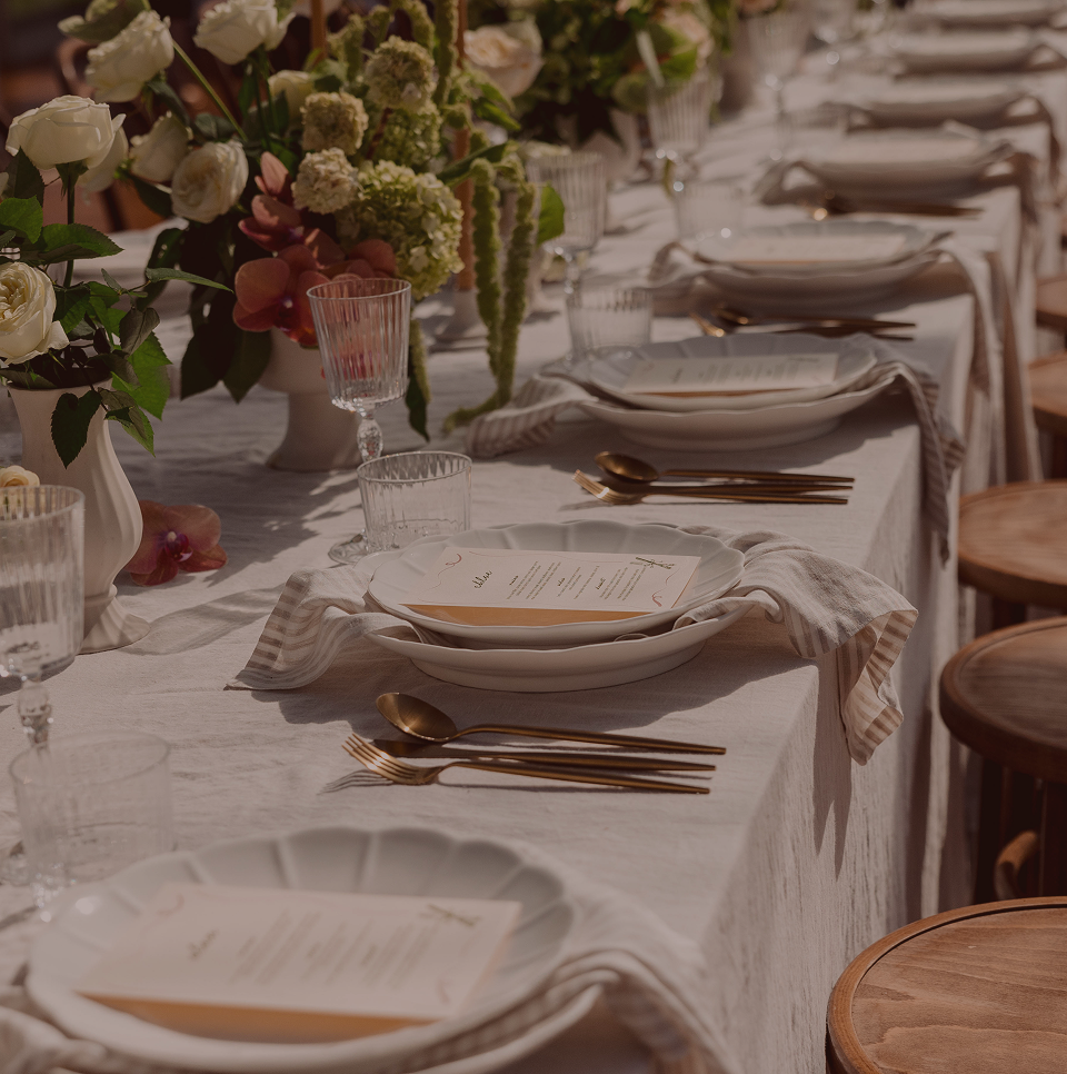 Elegant dining table set with white plates, gold flatware, and floral centerpieces.