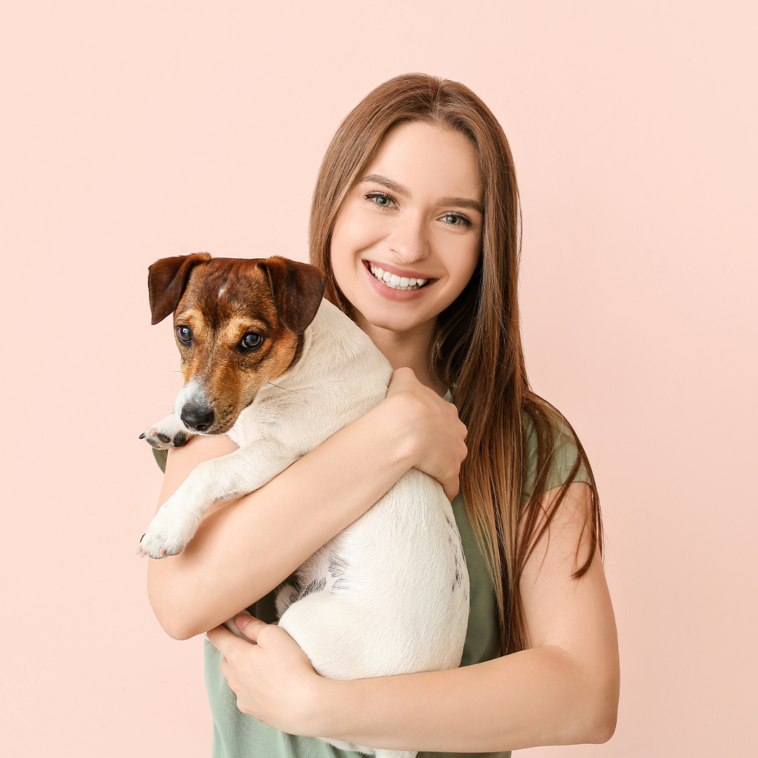 A woman smiling and holding a small brown and white dog with blue eyes against a pink background, Velvet studios ready made template