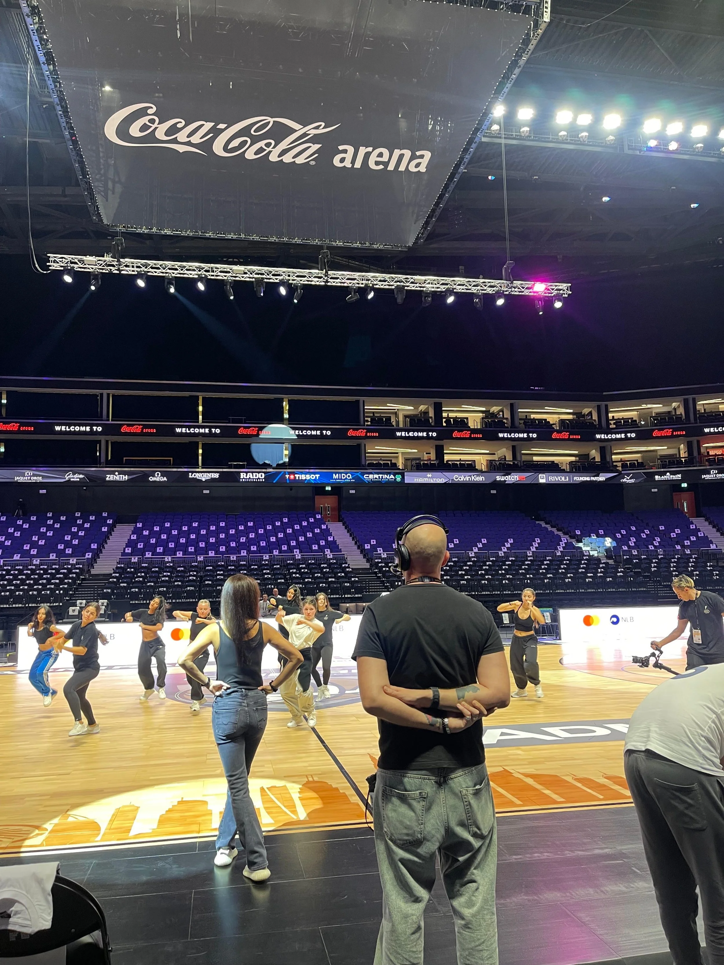 Performers rehearsing an in-game entertainment segment on court while the production team reviews the routine at Coca-Cola Arena.