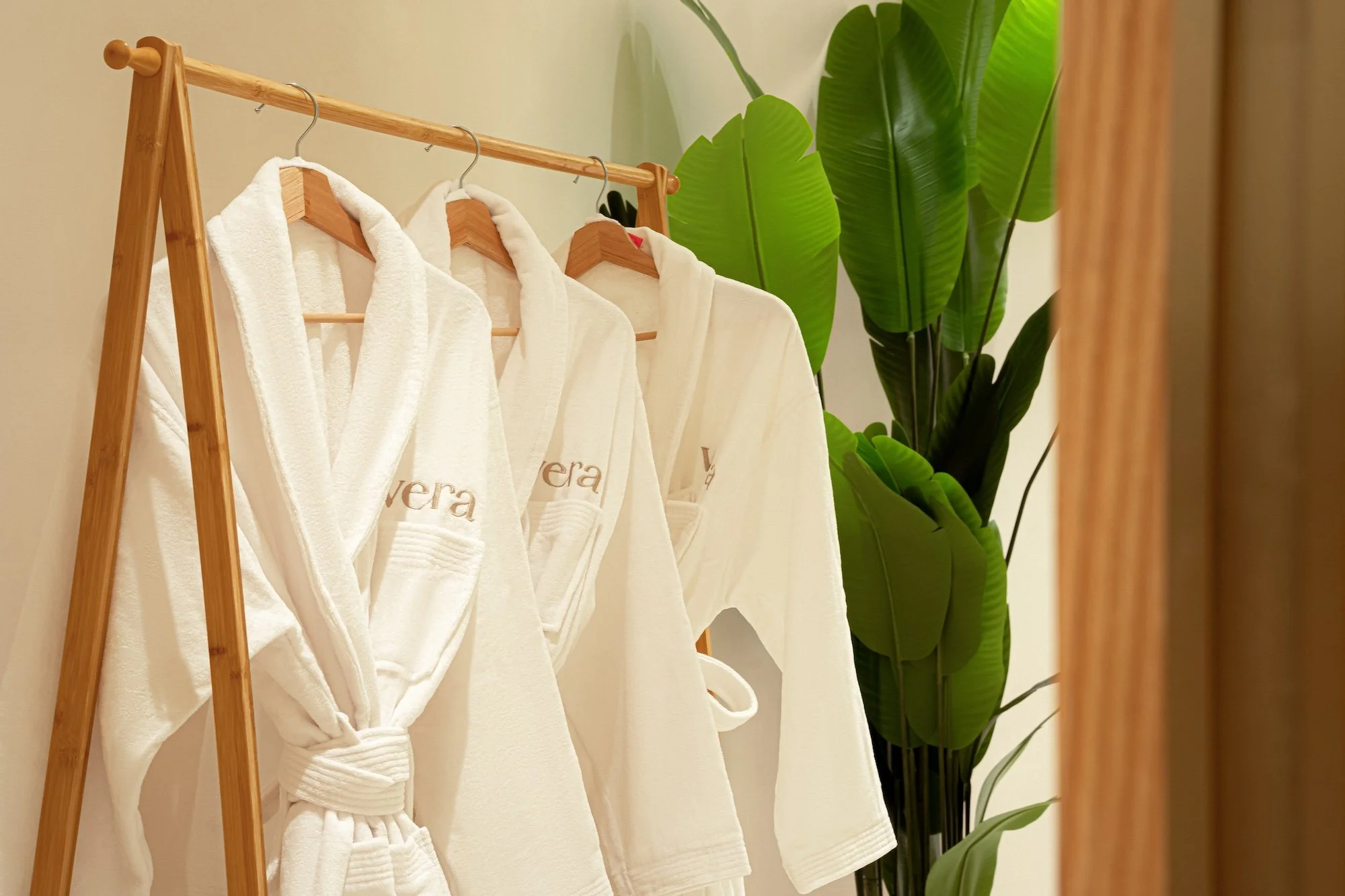 Vera Wellness robes displayed beside tropical greenery in the changing area.